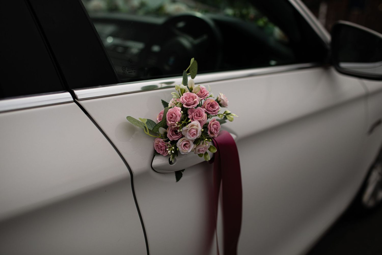 Pink roses bouquet tied with burgundy ribbon decorating a white wedding car door.