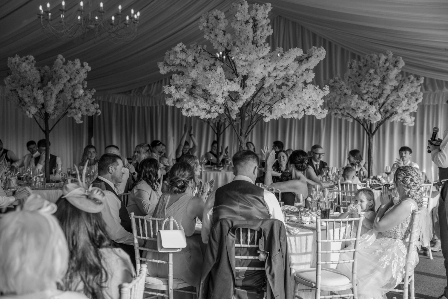 Elegant black and white wedding reception in a marquee with floral tree centerpieces and guests seated at decorated tables.