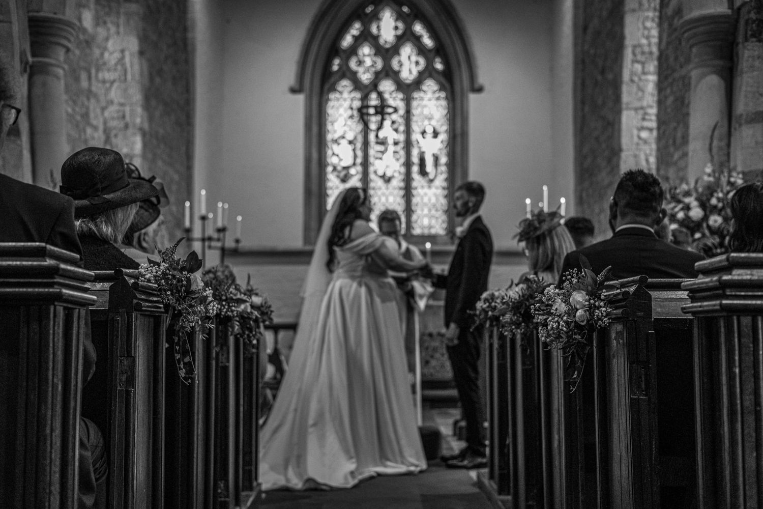 Black and white photo of a bride and groom at the altar in a historic church with stained glass windows.