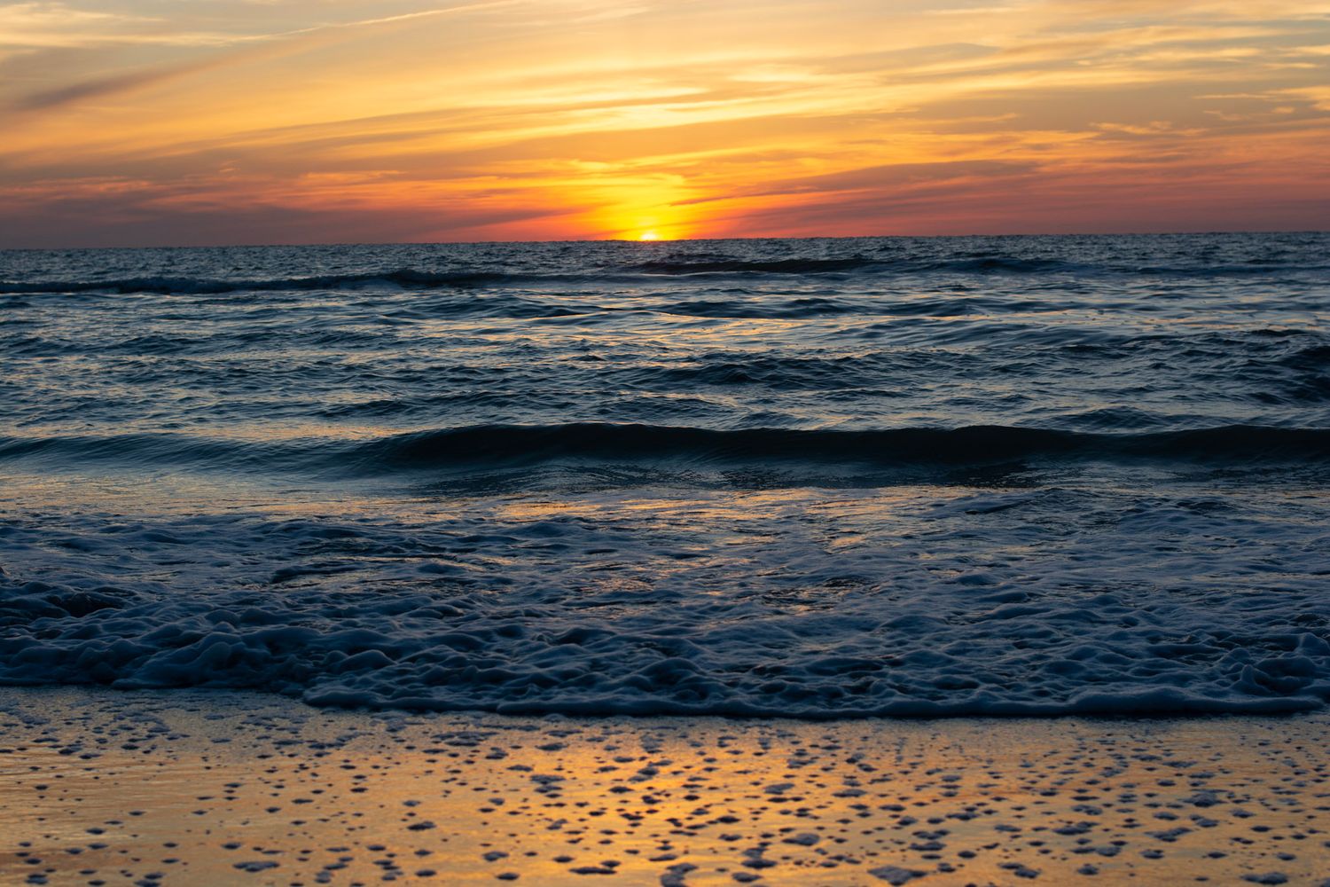Stunning orange sunset over ocean waves crashing on a sandy beach during golden hour. St Pete beach photographer
