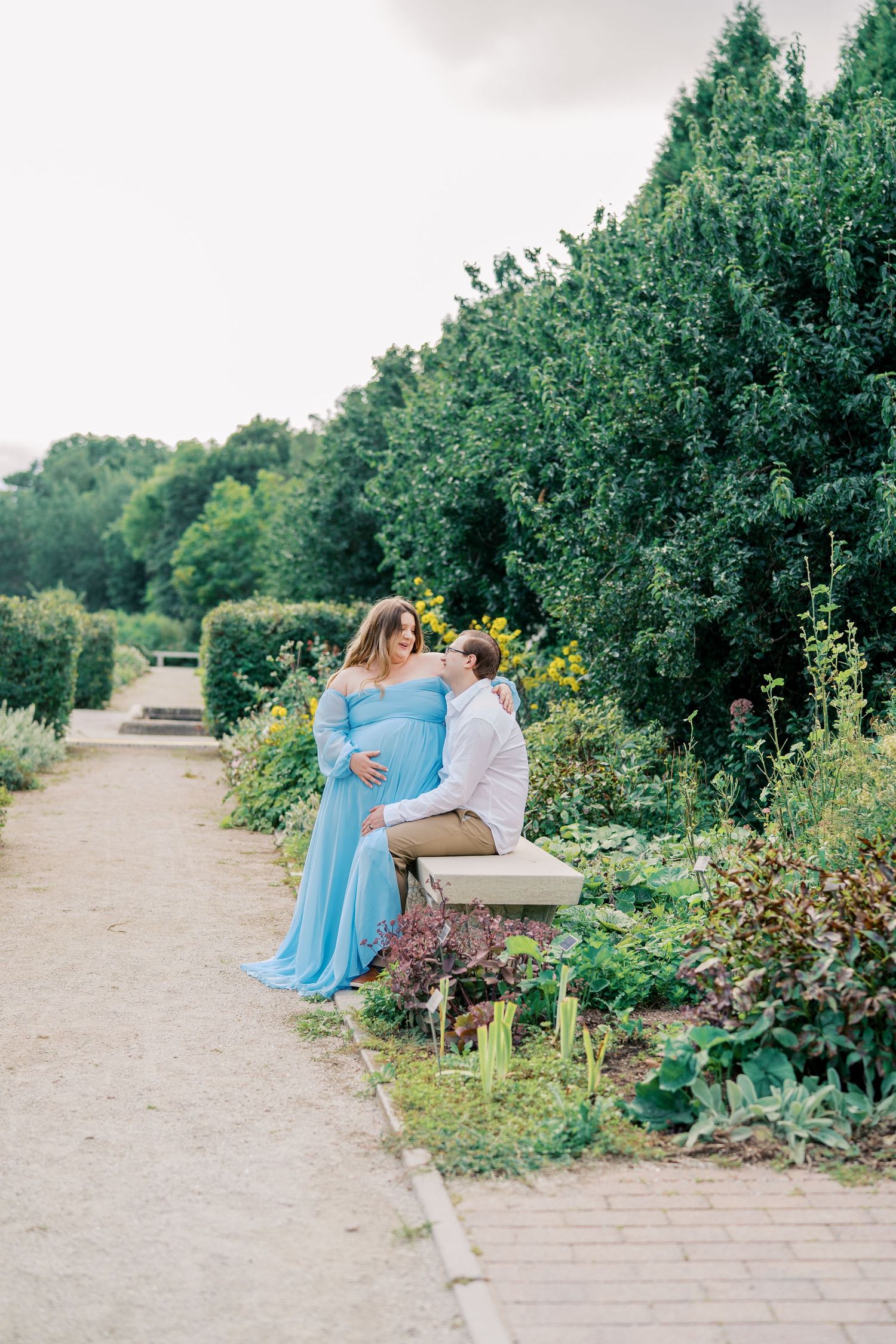 Couple sitting on bench in beautiful garden path surrounded by greenery.