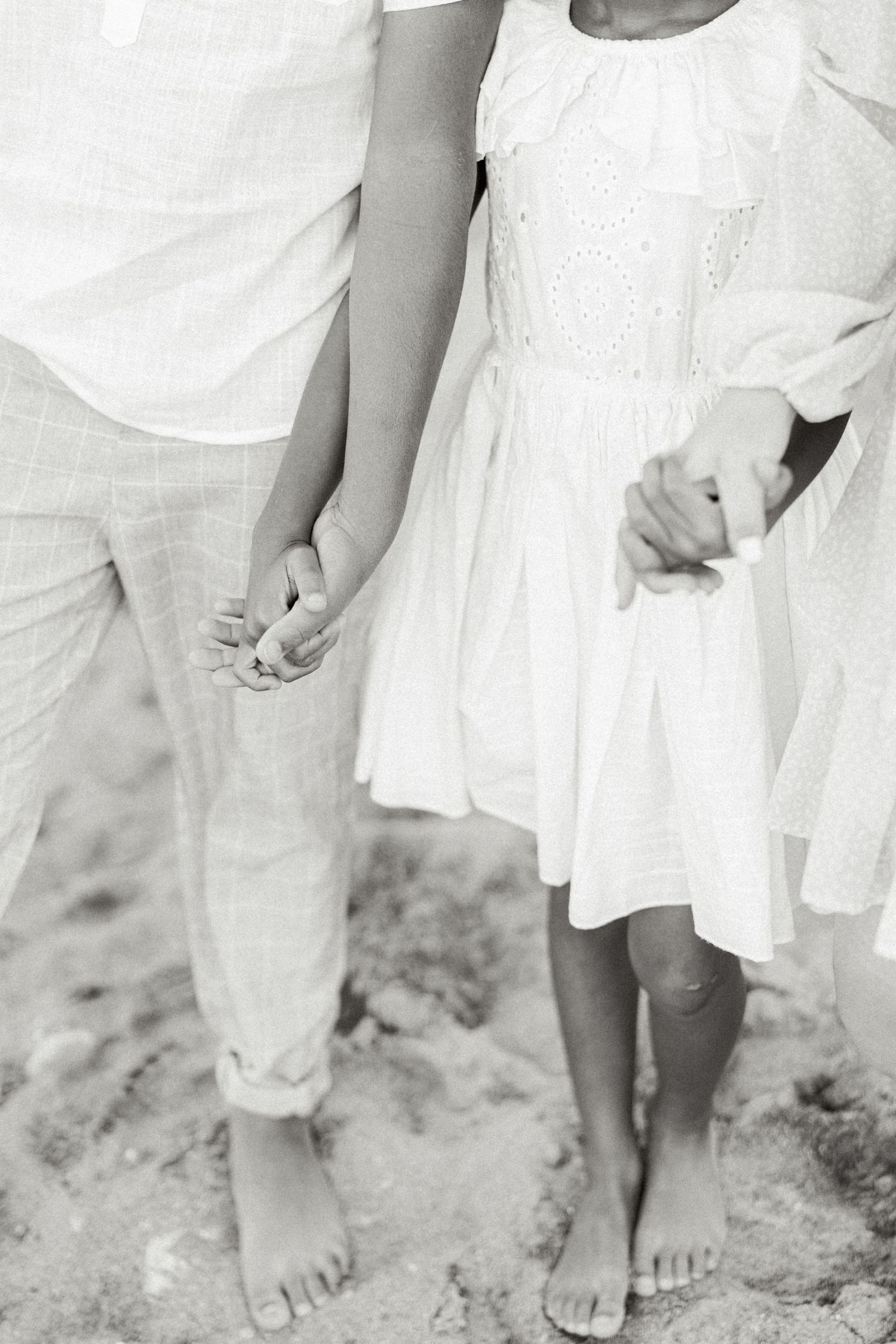Two pairs of bare feet standing together on sandy ground with white clothing visible.