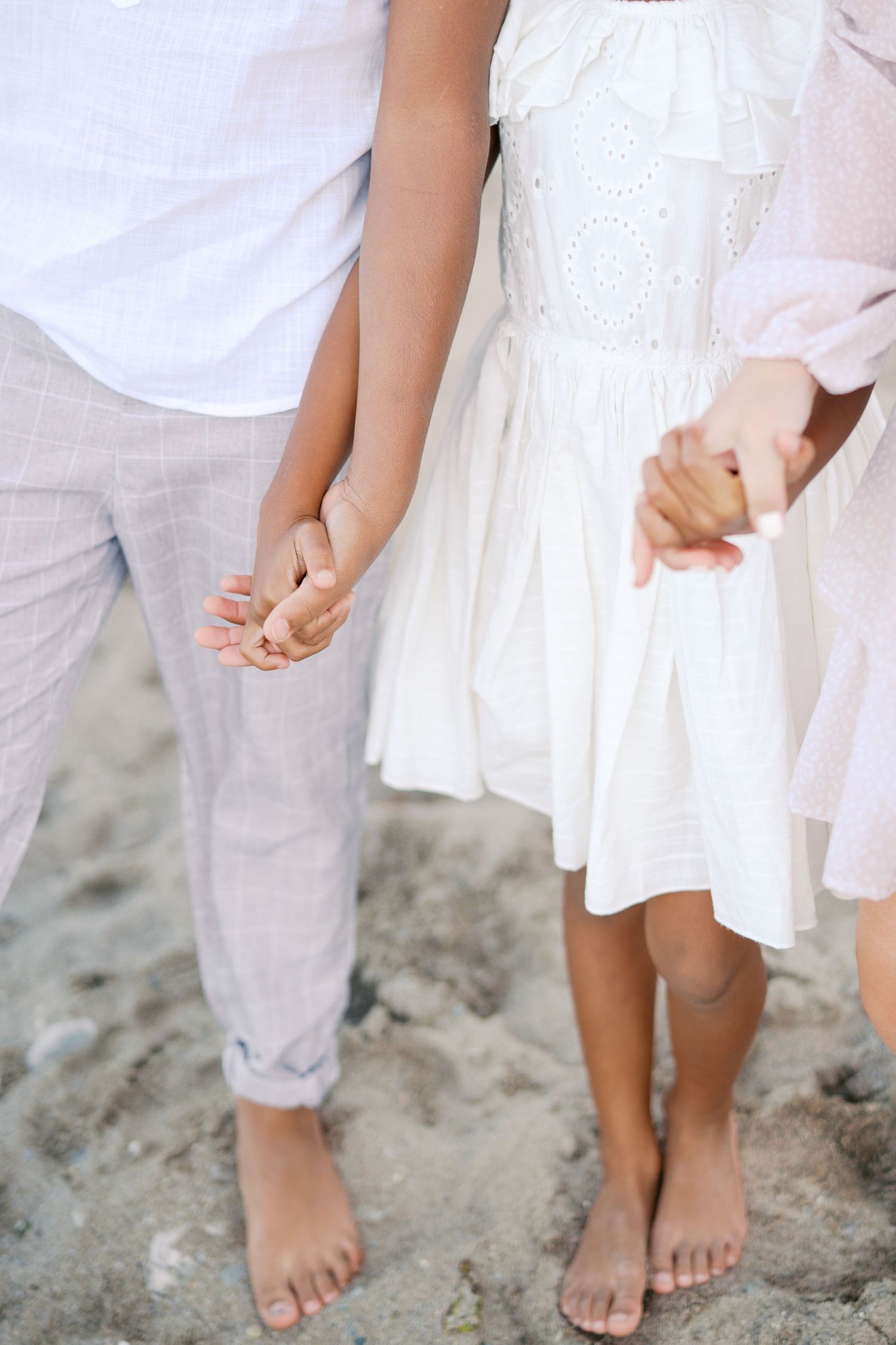 Close up of bare feet and white dress on sandy beach.