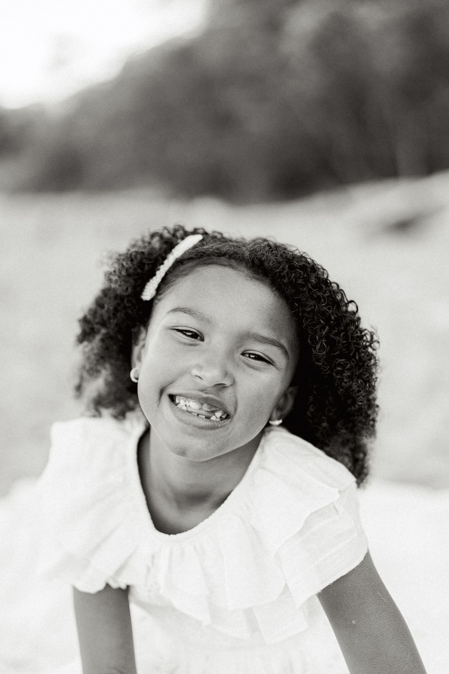 A child in white clothing smiles brightly in black and white portrait series.