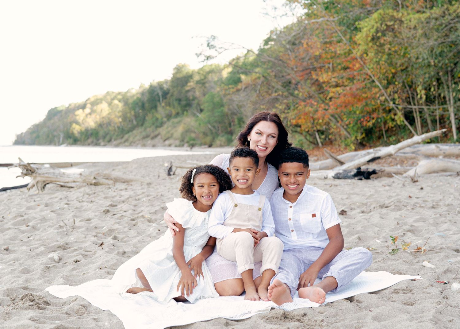 Family group relaxing together on a sandy beach wearing white clothing.