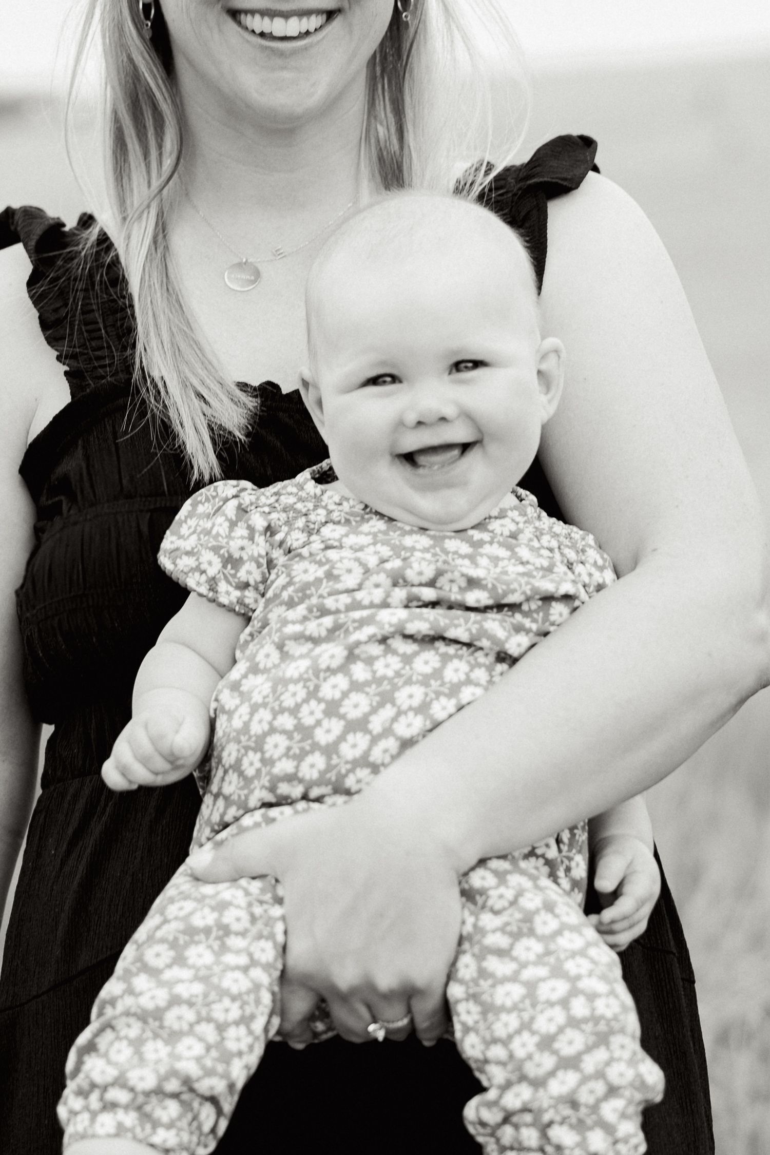 Black and white portrait of a happy baby wearing a polka dot outfit being held in loving arms.