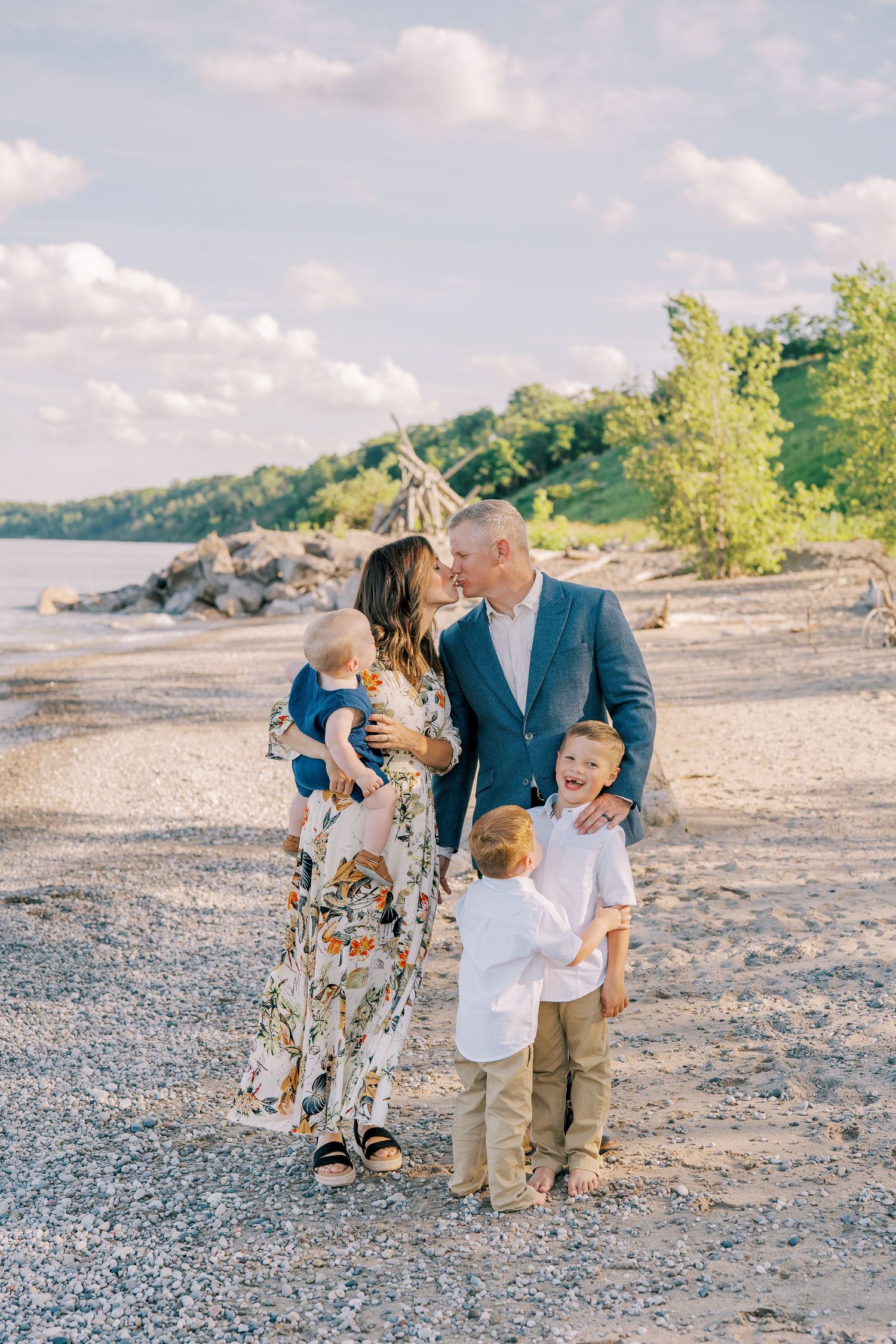 Family enjoying a sunny day together on a rocky beach with water and trees in background.