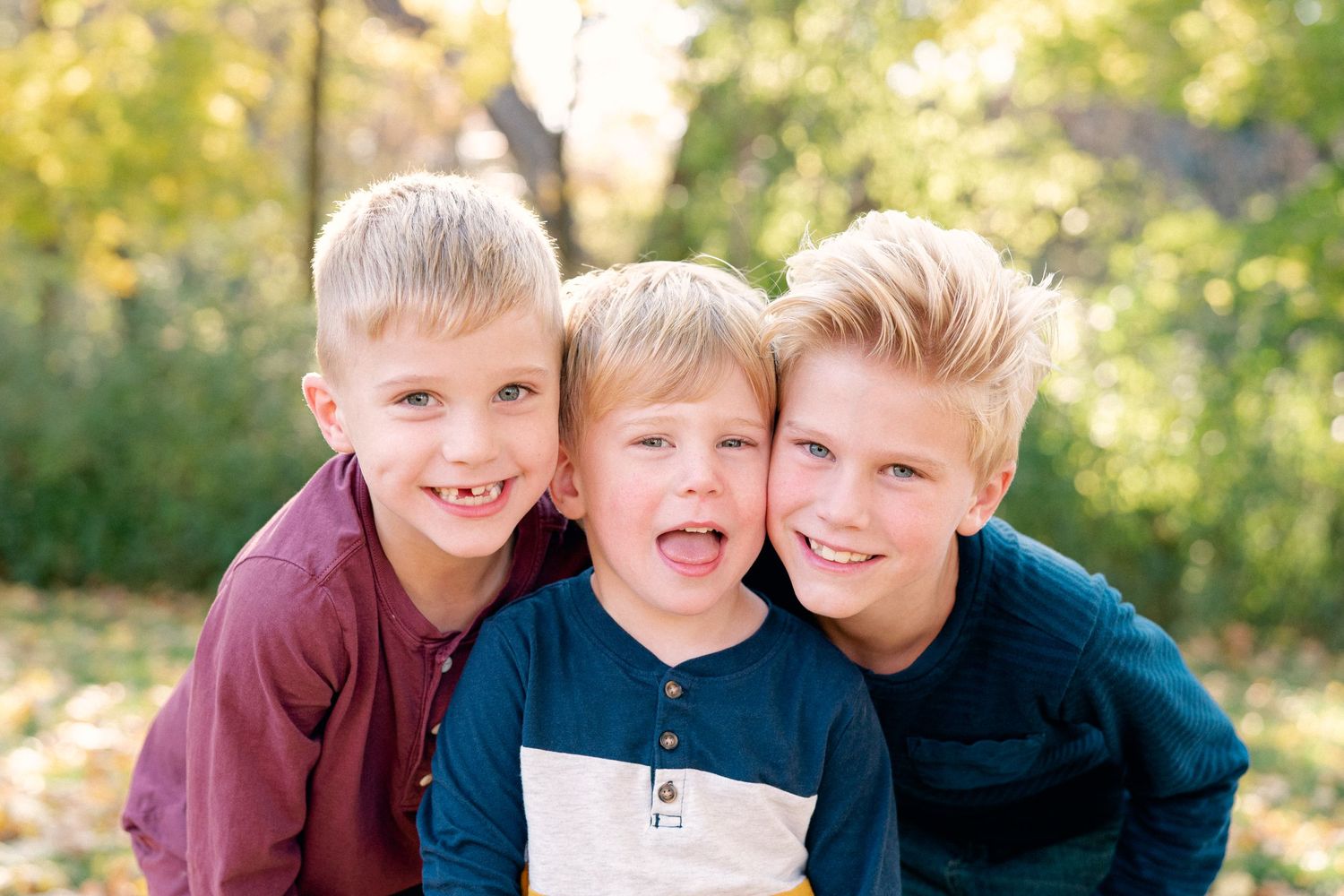Three young boys smiling together outdoors in autumn setting.