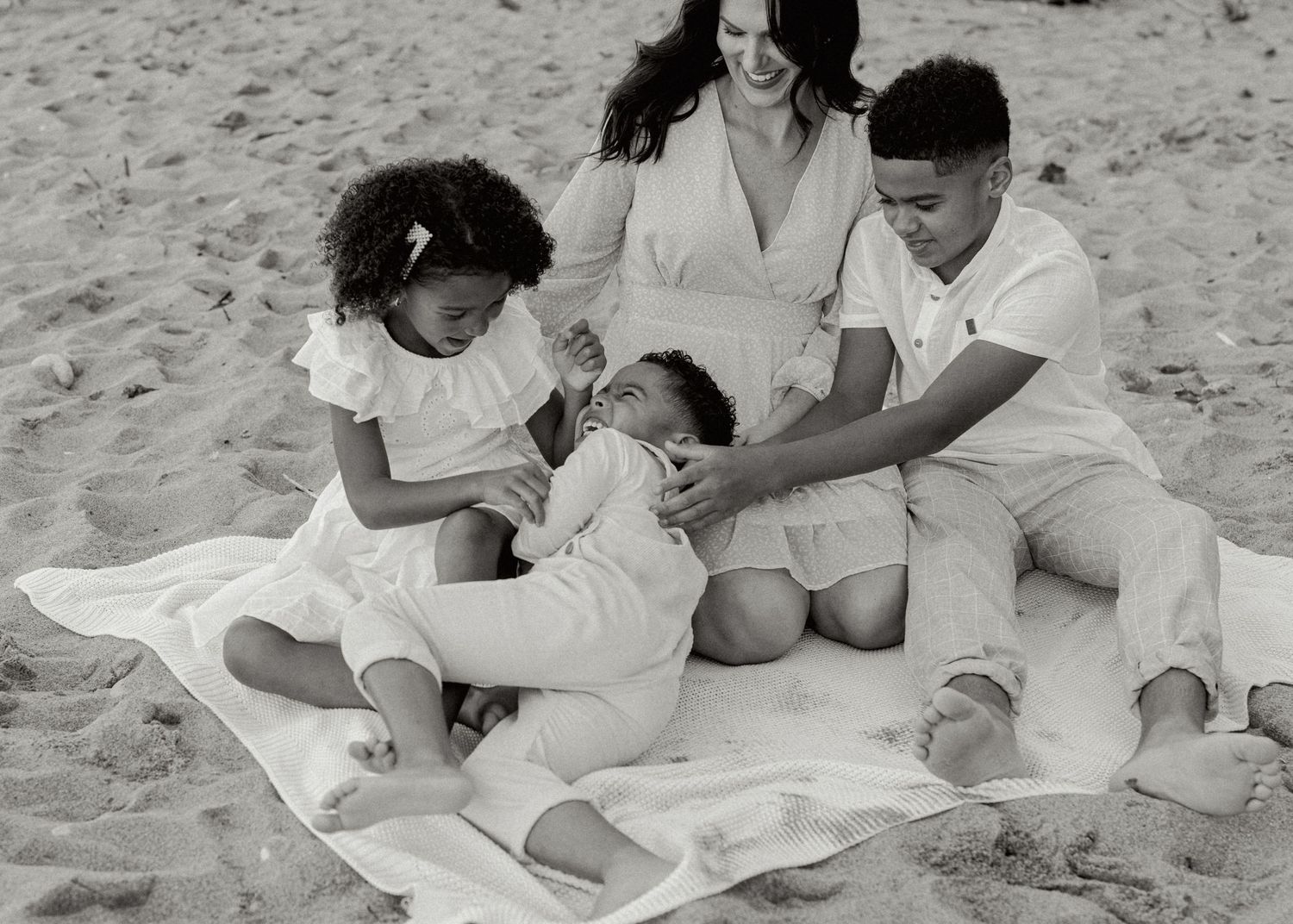 A black and white photo shows a family sharing playful moments together on a beach blanket.