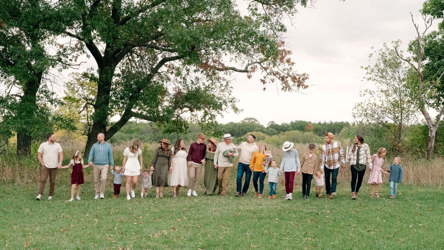 Large extended family group photo taken outdoors in coordinated neutral outfits.