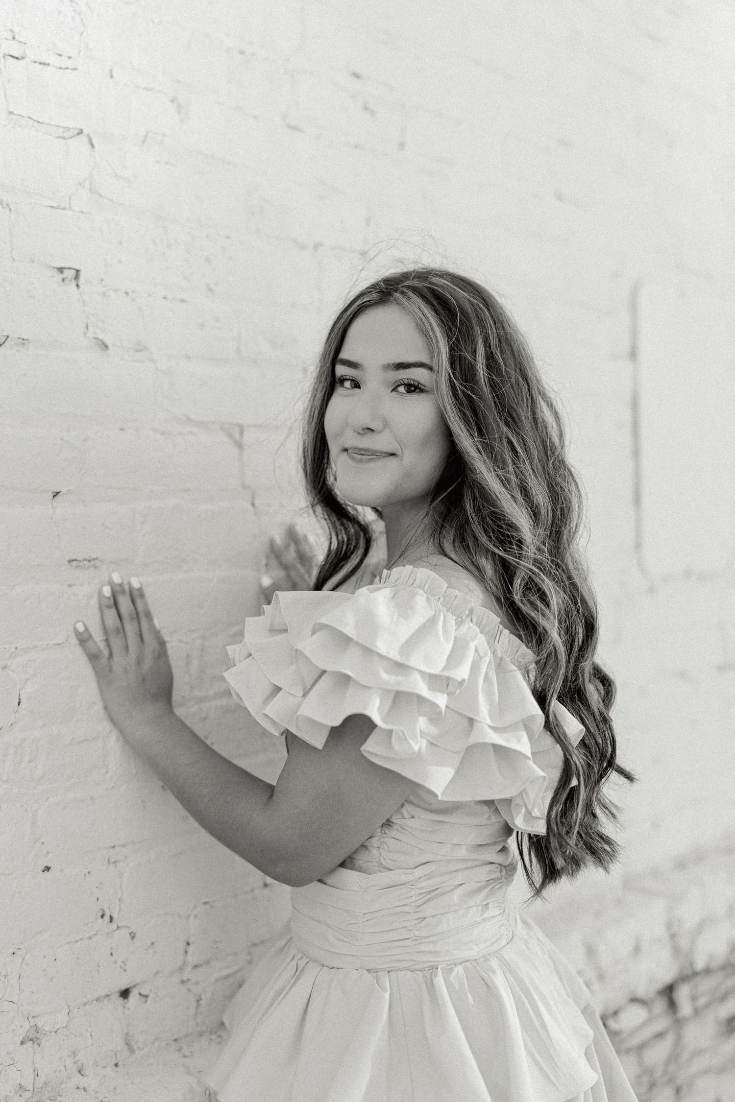 Artistic black and white portrait series against a white brick wall featuring a ruffled dress.