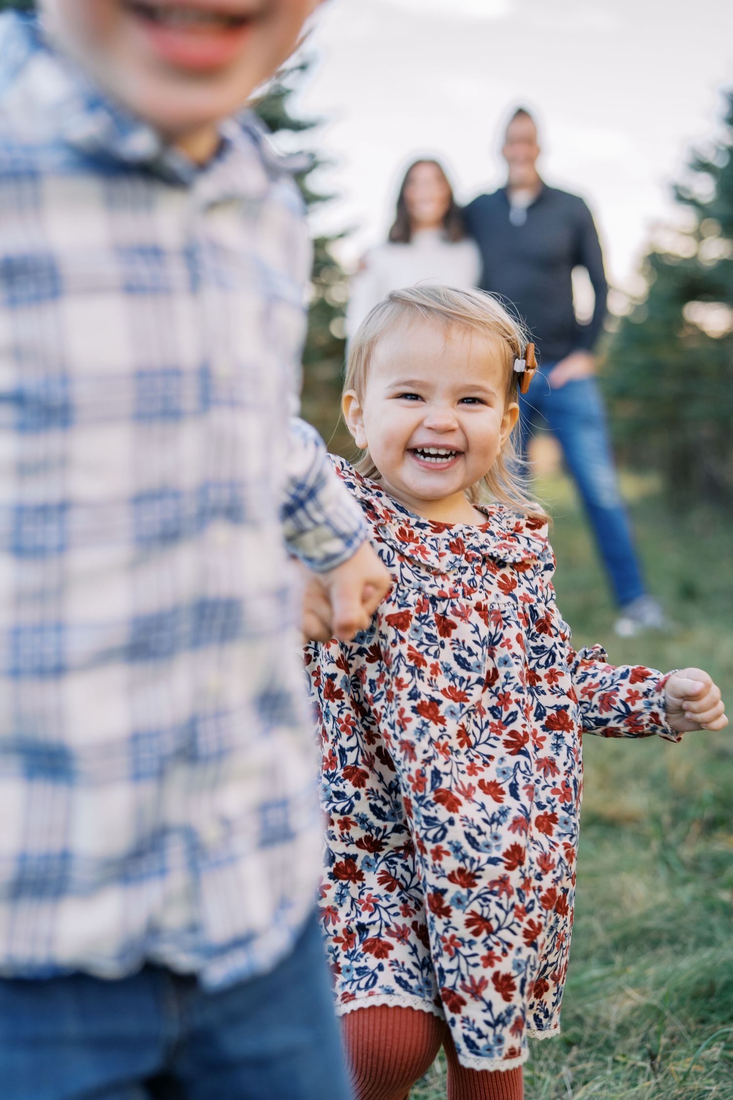 Joyful toddler in floral outfit playing outdoors with family in background.