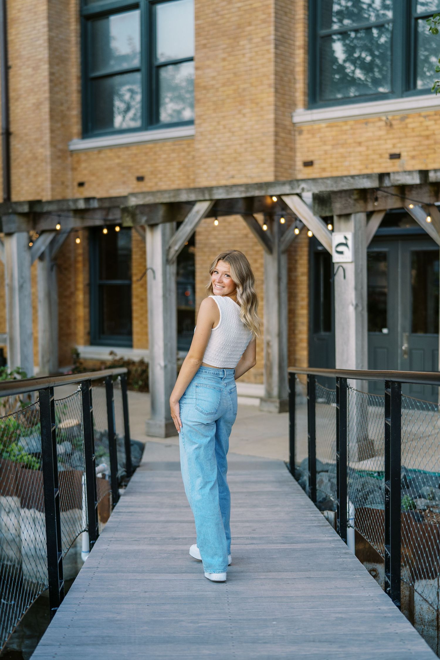 A person in casual attire walking on a wooden bridge against a brick building backdrop.