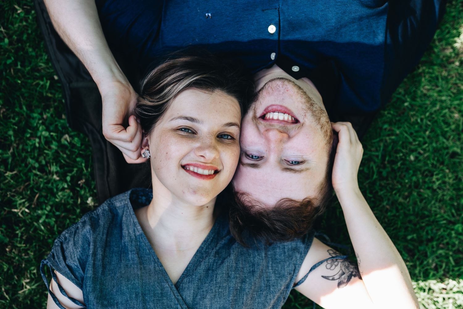 A couple lying in grass wearing denim and smiling together on a sunny day taken by Melbourne couples photographer peiauiphotography
