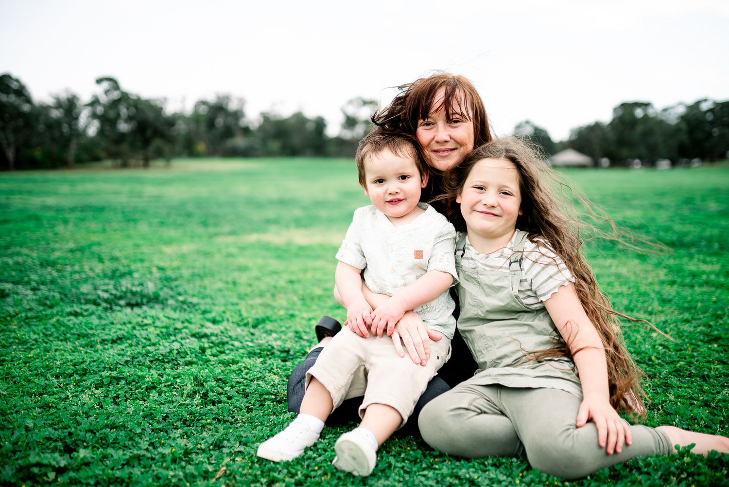 Family sitting together on bright green grass lawn at outdoor park on sunny day taken by Melbourne family photographer