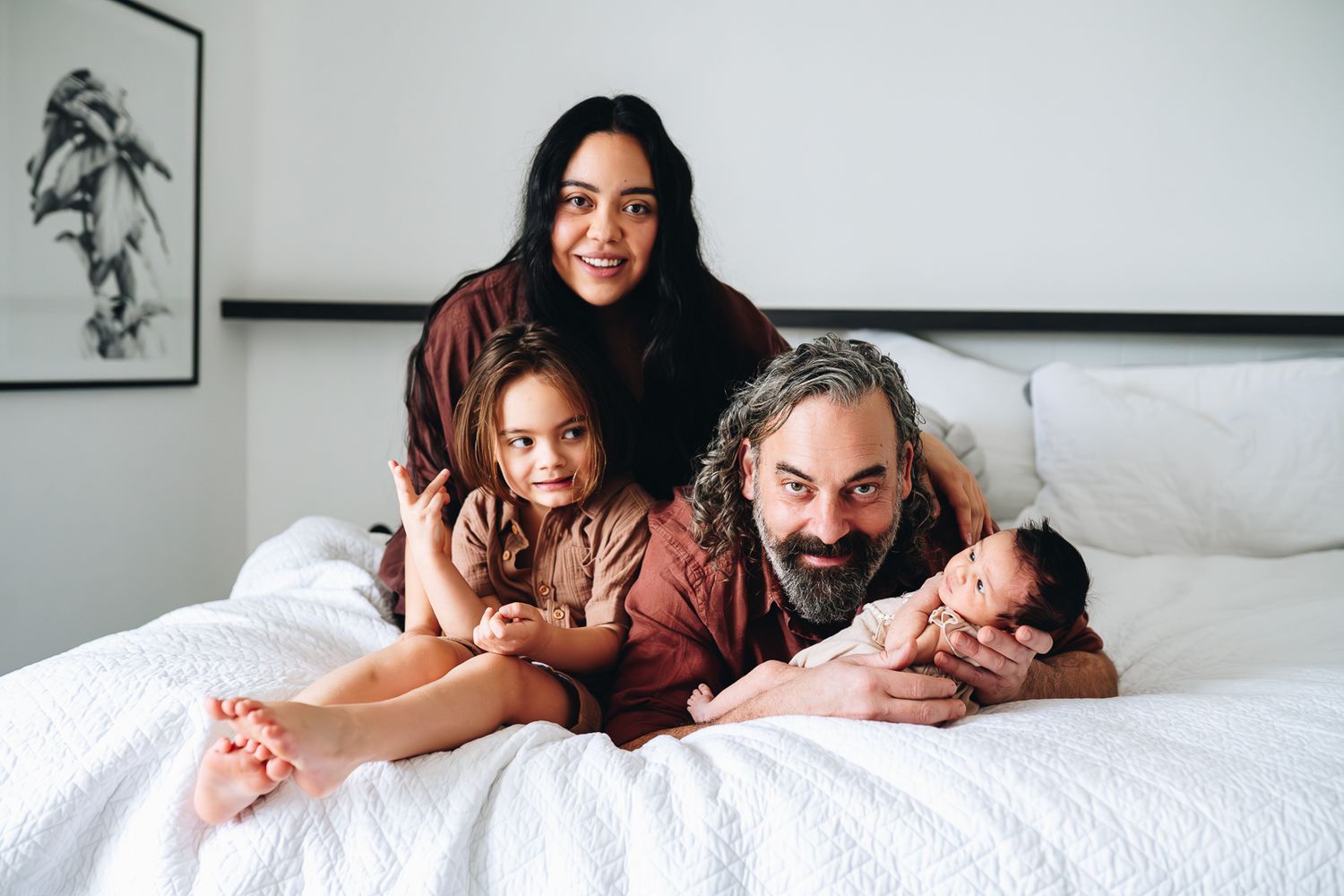 A family shares joyful moments together while relaxing on a white bed in a room taken by Melbourne newborn and family photographer.