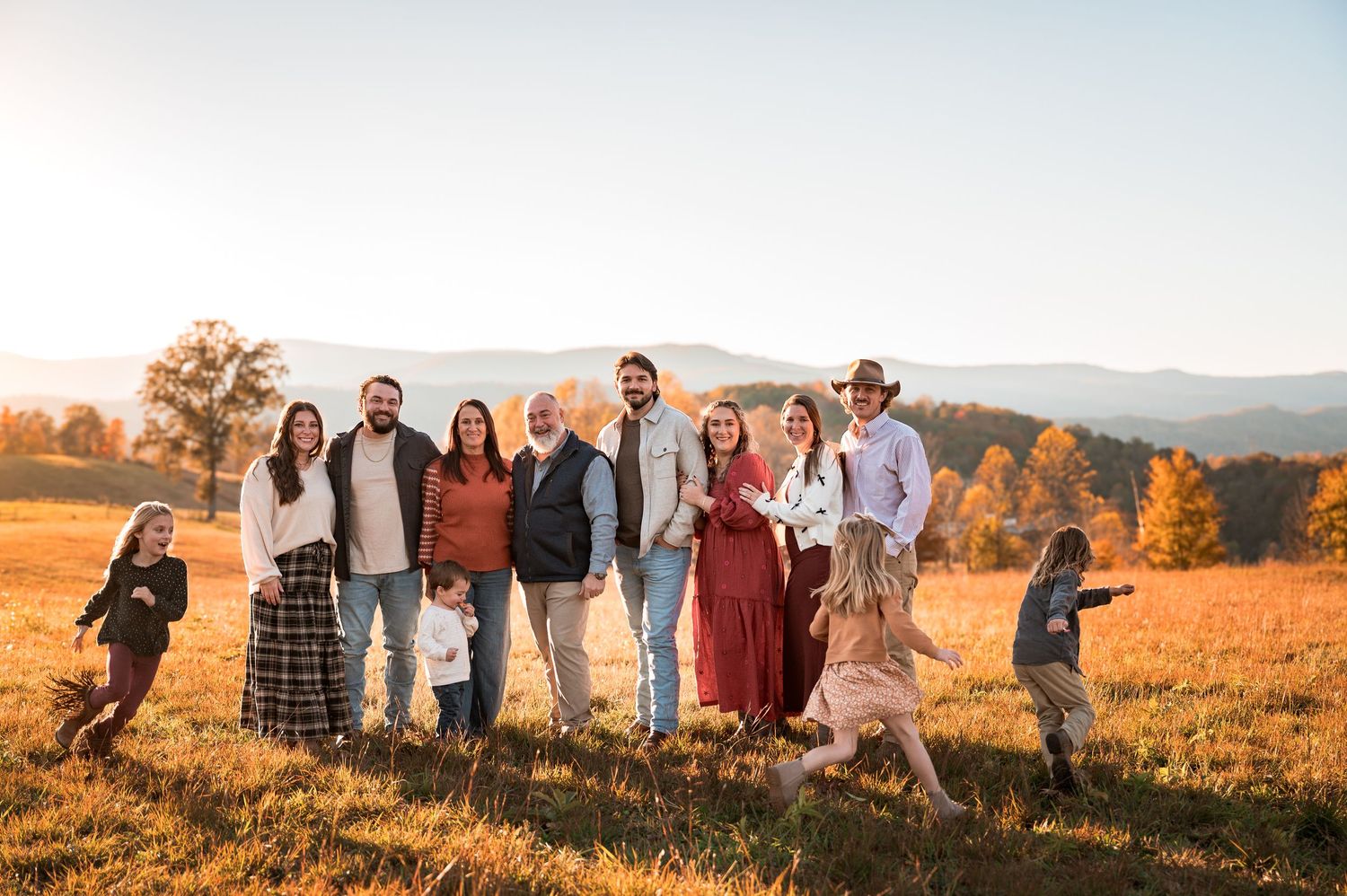 A group poses together in a golden autumn field during sunset with mountains in the background.
