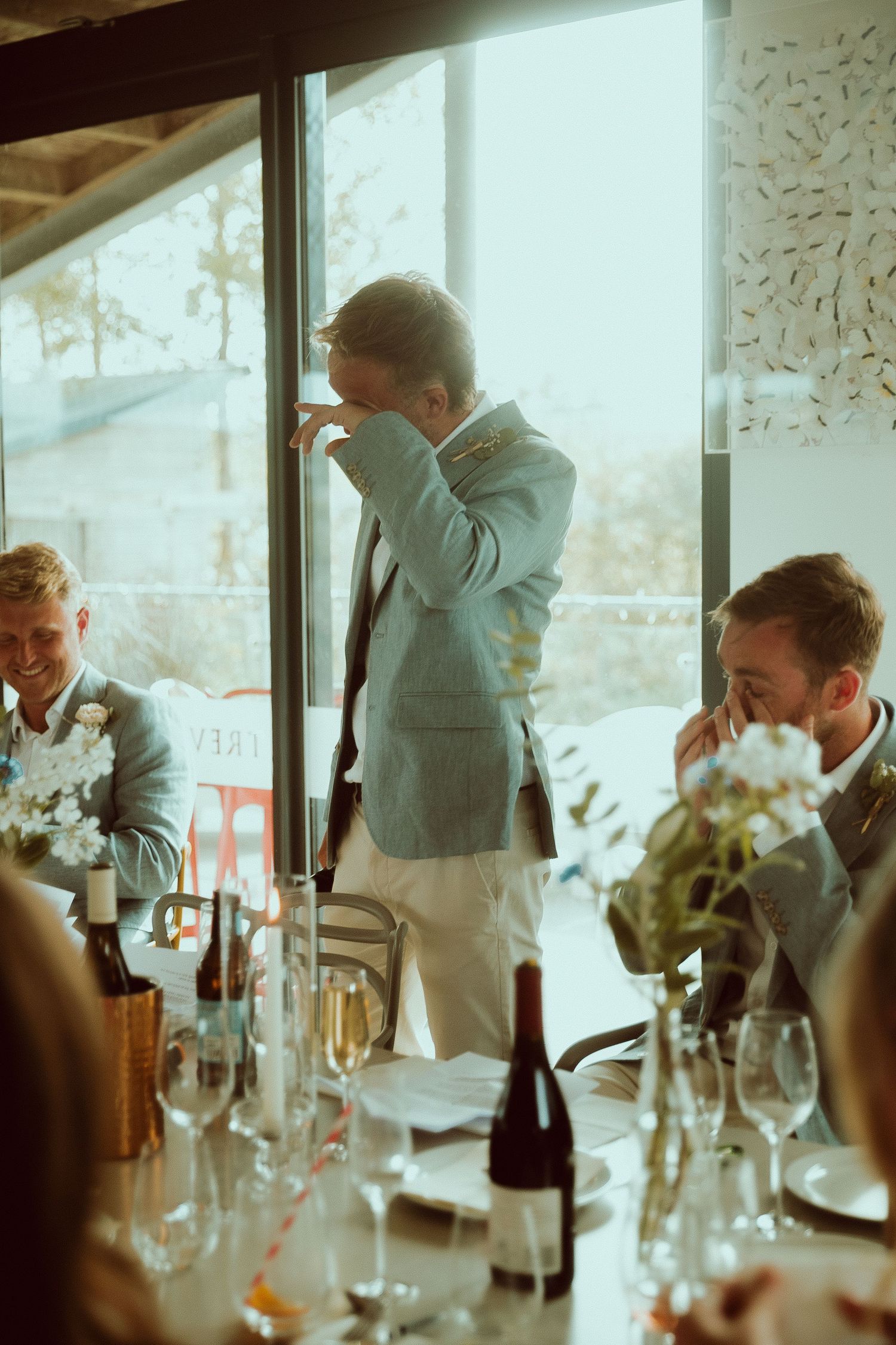 Man in light blue suit giving a toast at an elegant wedding reception dinner table with wine glasses.