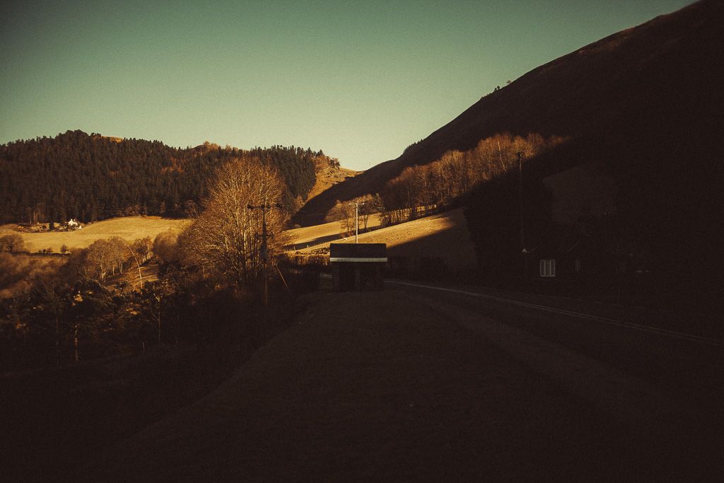 A dark moody rural road winds through Wales in autumn trees with mountain hills in the background at dusk.
