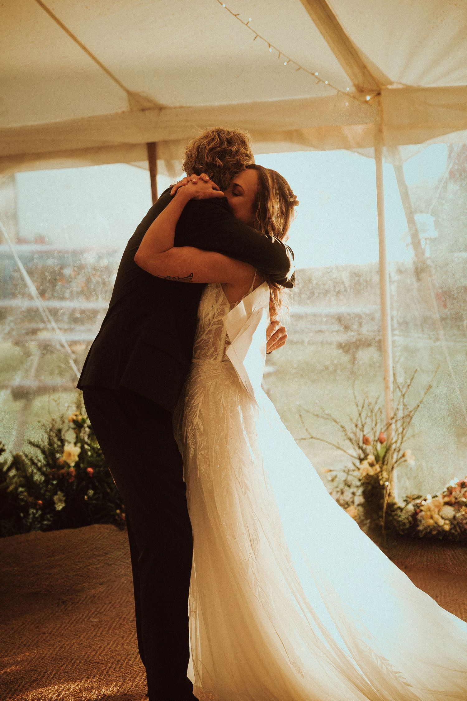 A bride and her dad share an embrace after a speech inside an elegant white tent wedding venue.