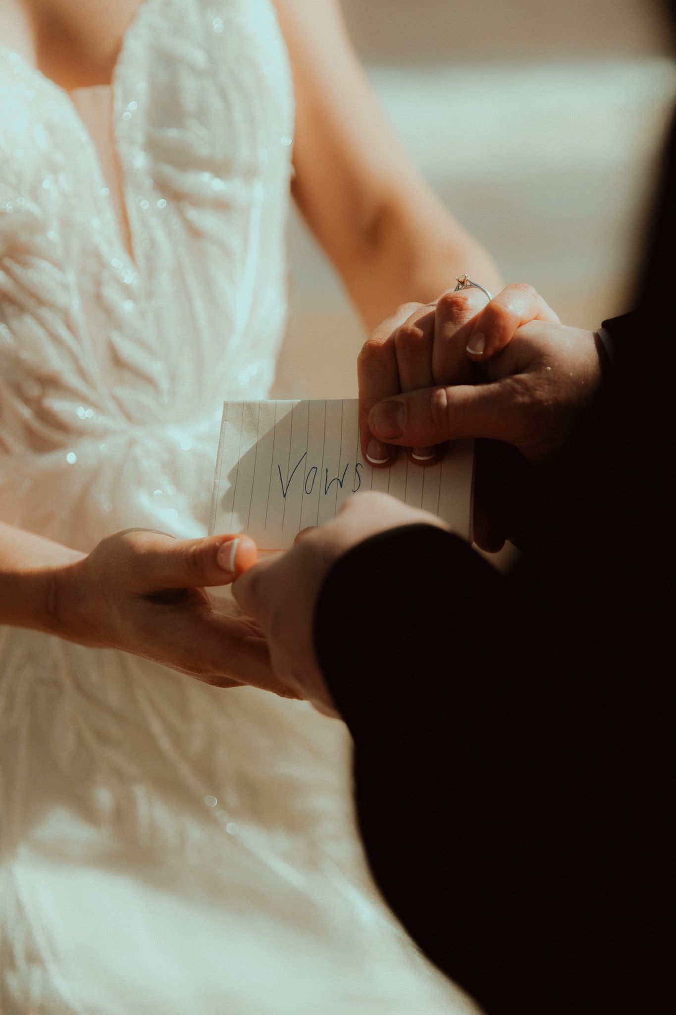 Bride and groom holding a small card with wedding vows written on it during their ceremony.