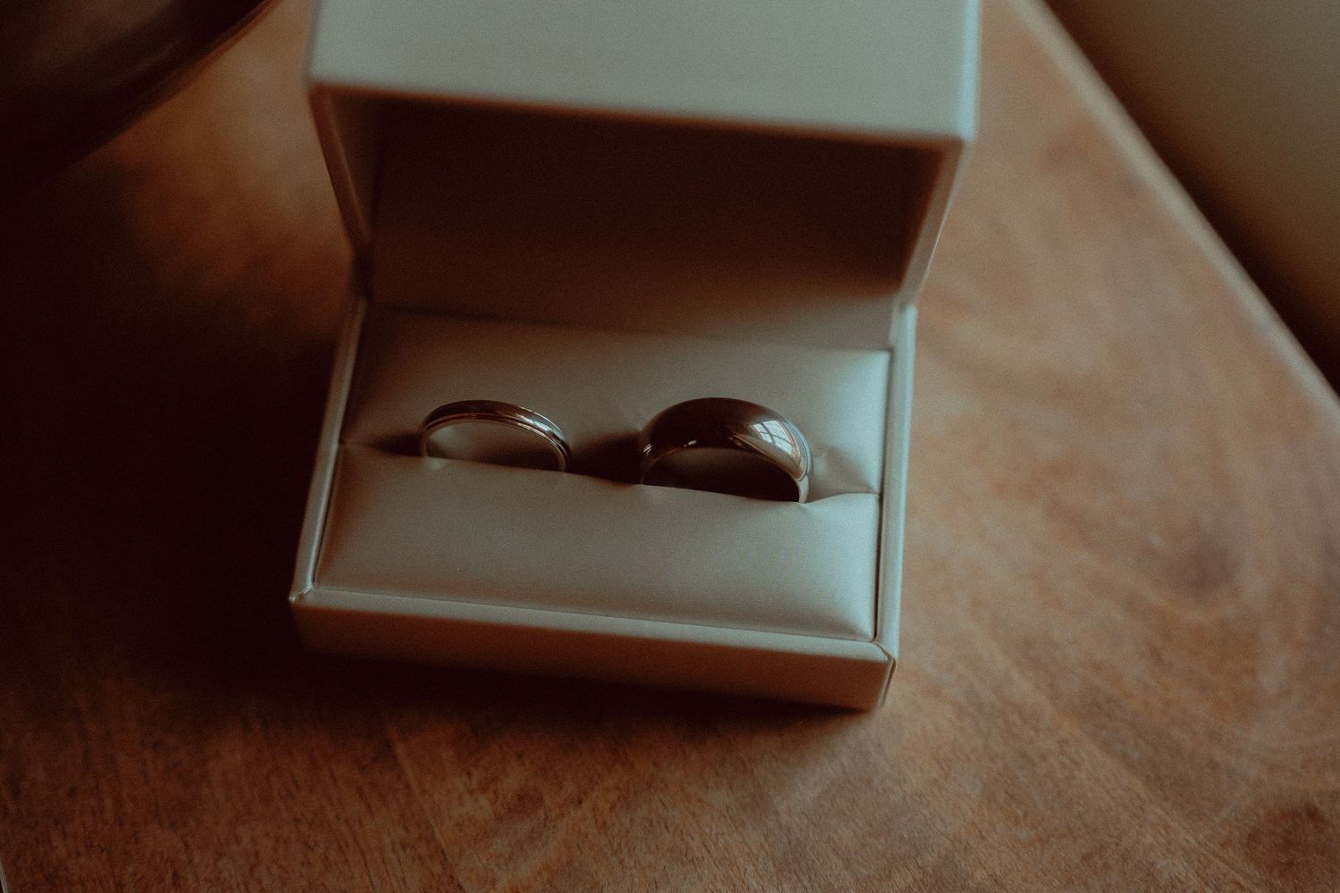 Two gold wedding bands displayed in an open white ring box on a wooden table.