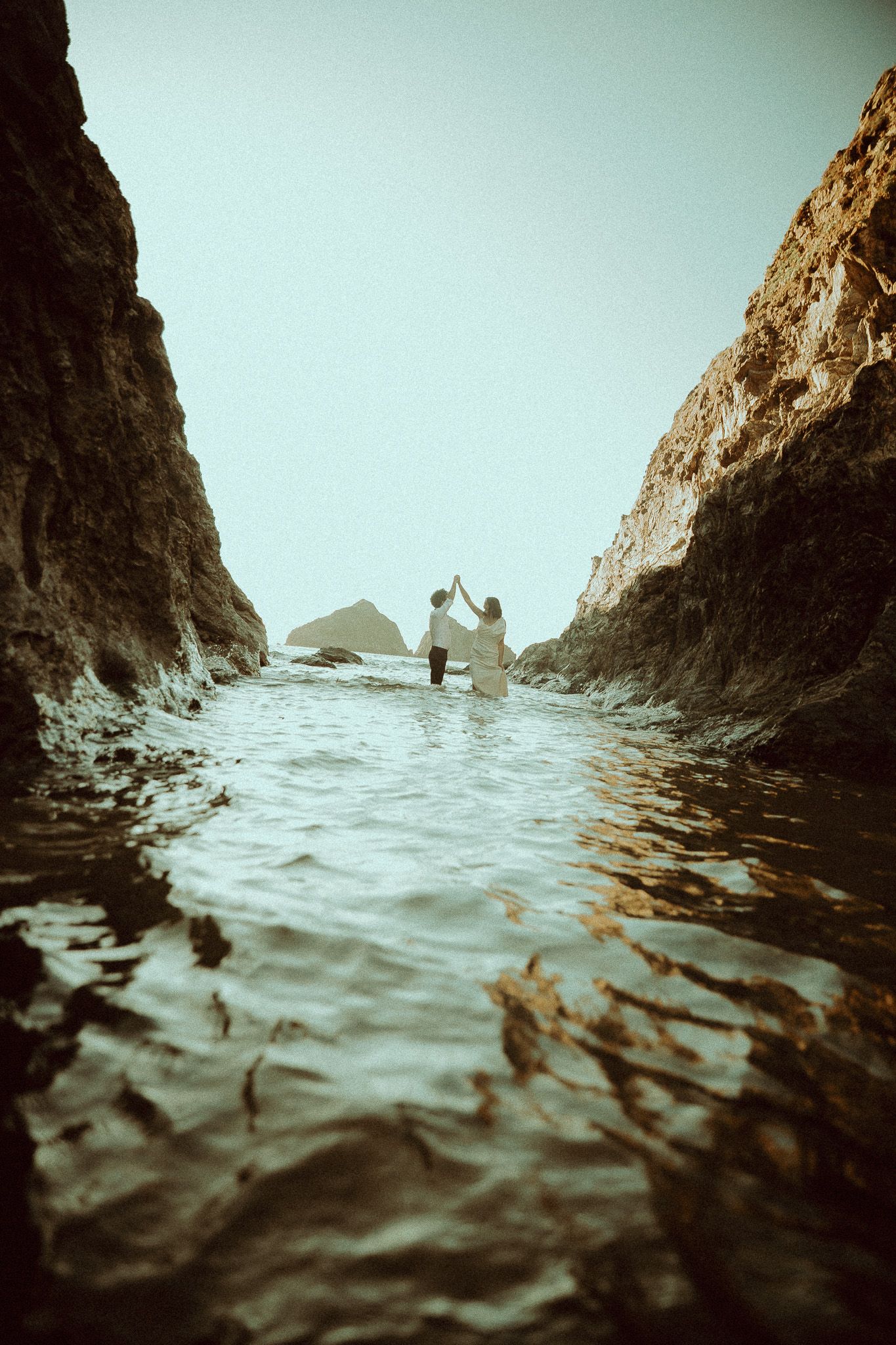 Dramatic seascape through rocky cliffs with waves and silhouettes in the misty distance captured from water level.