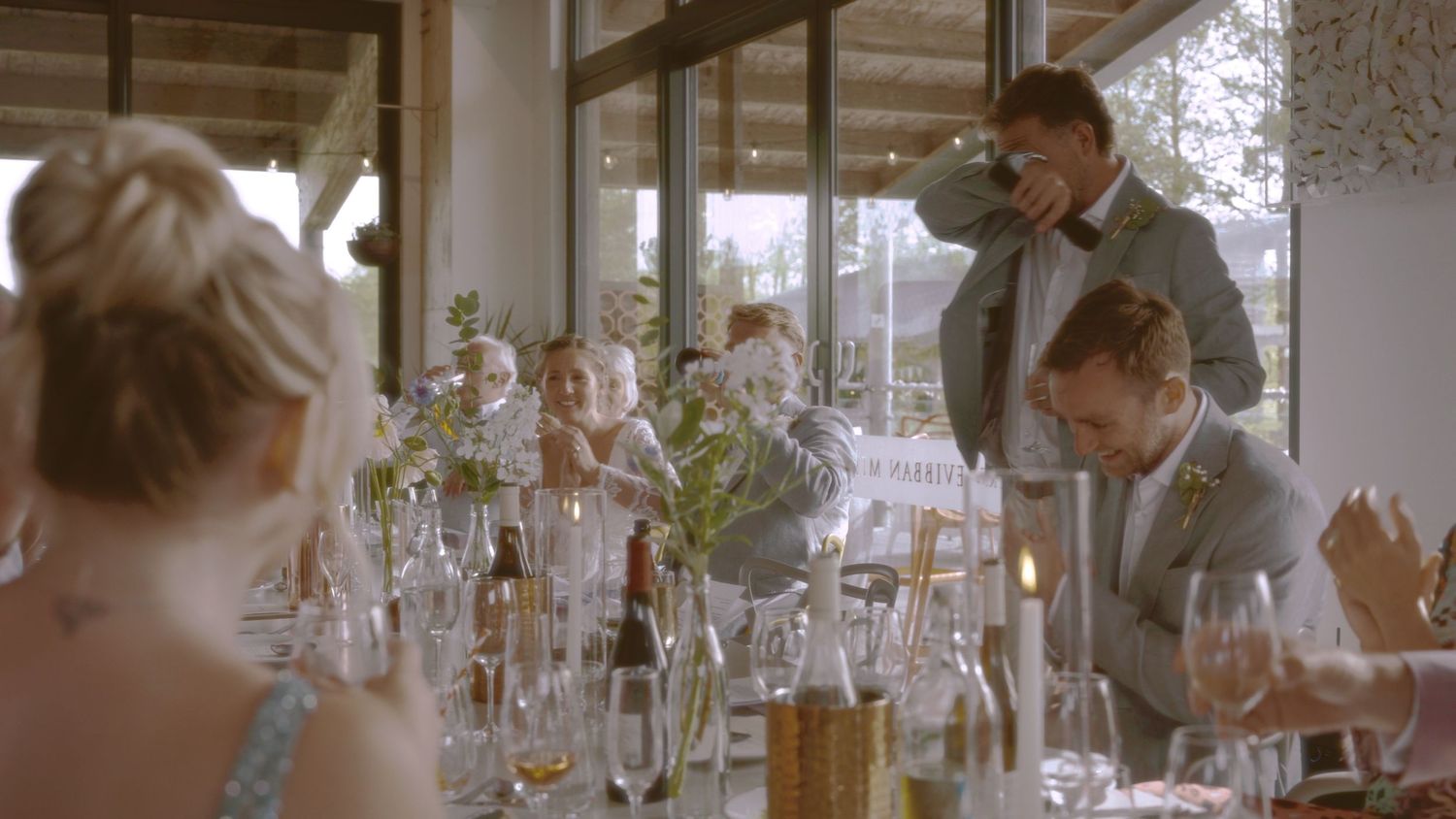 Elegant wedding reception with guests seated at decorated table, man in suit toasting with champagne glass.