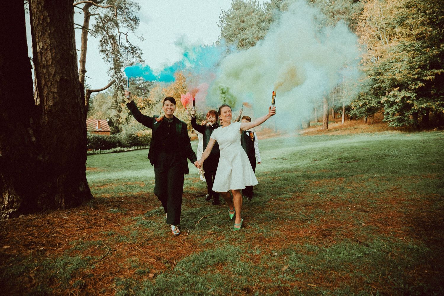 A couple celebrates with blue smoke bombs in a scenic autumn park setting during a photo session.