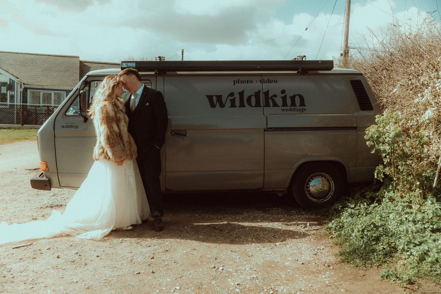 Newlywed couple kissing beside a vintage Wildkin VWt25 van, Big grey, on their wedding day, bride in white gown with fur stole.
