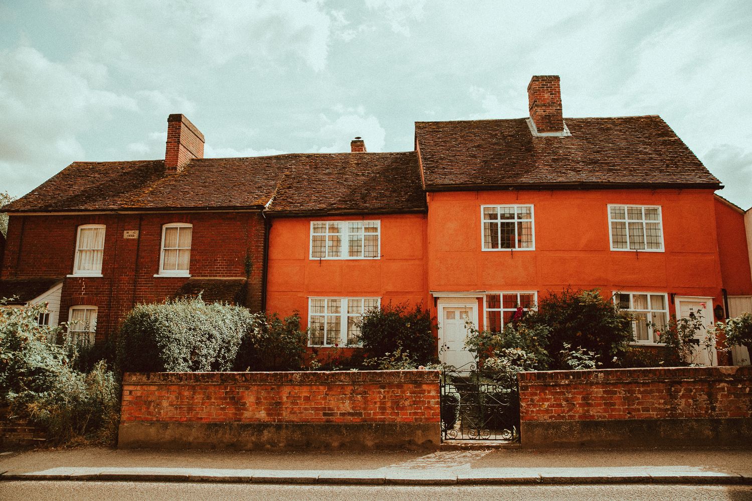 Charming red and orange terraced houses with white windows and brick wall garden in an English village street.