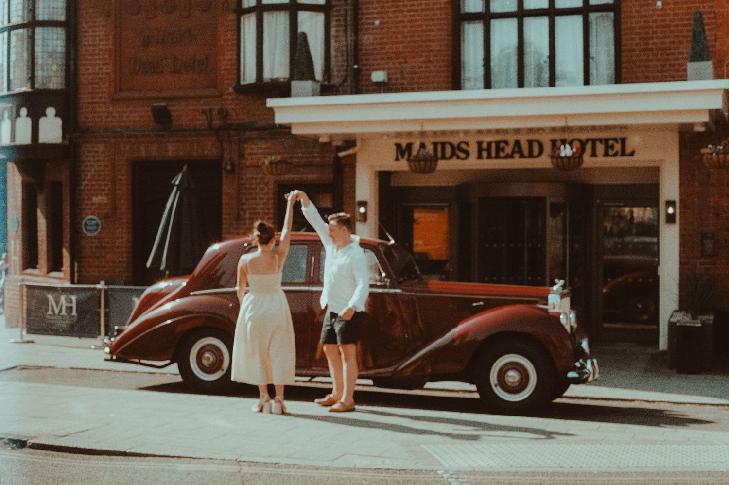 Couple dancing outside the historic Maids Head Hotel with a vintage red car in Norwich, UK.