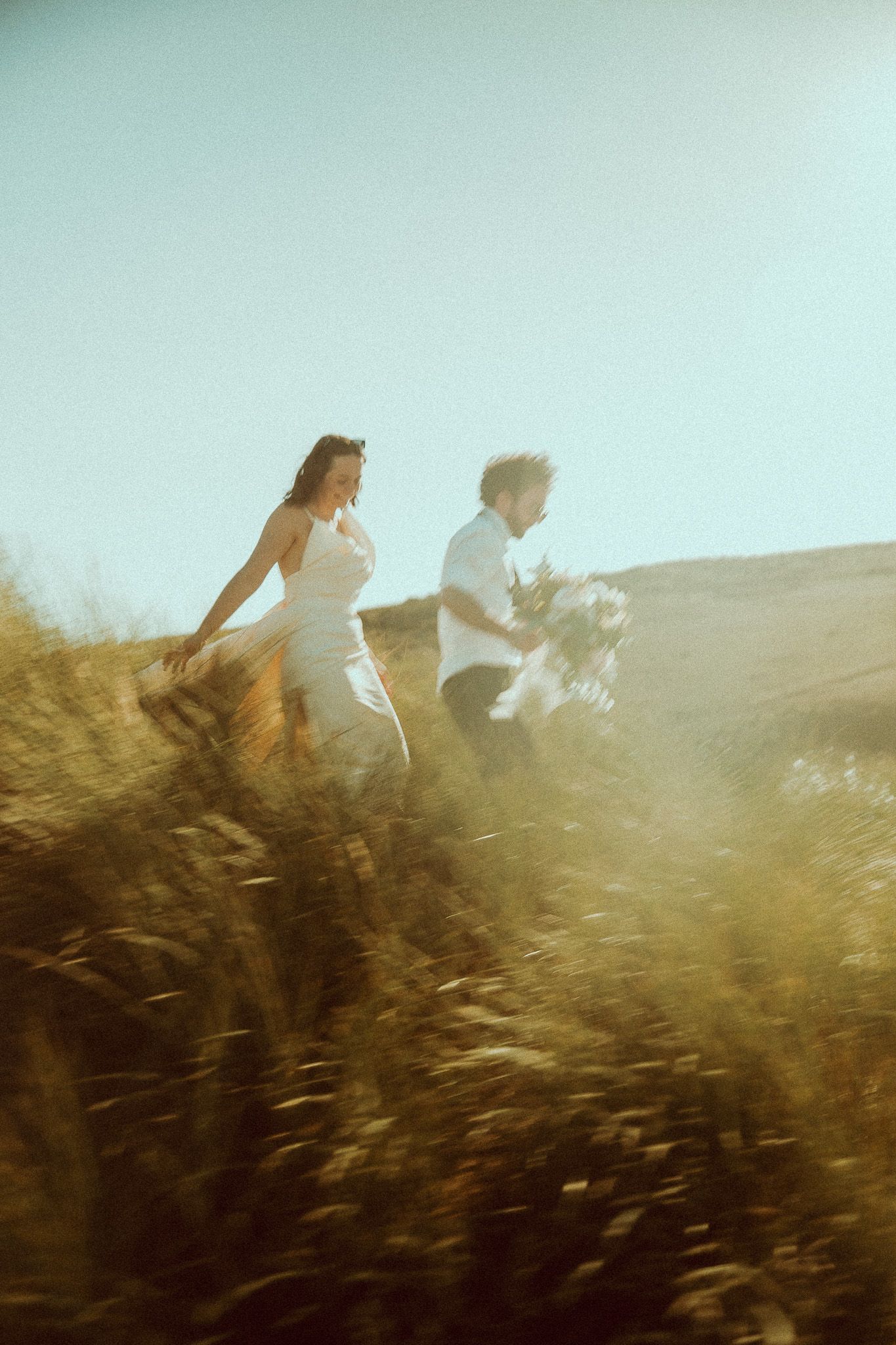 Two silhouettes run through a sunlit field of tall grass creating a dreamy, ethereal atmosphere at golden hour.