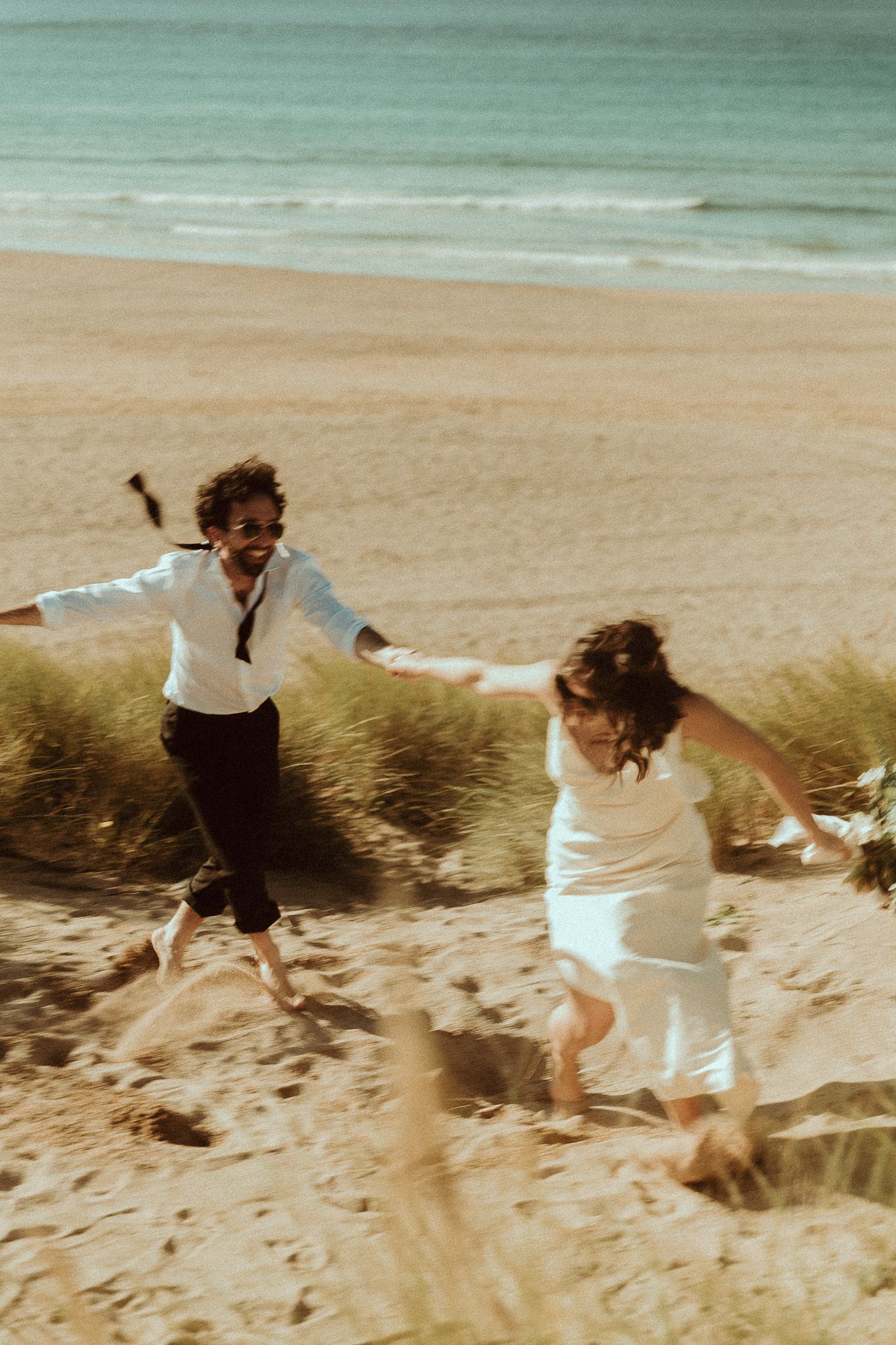 A sequence of photos showing two people running and jumping down a sandy beach dune near the ocean.