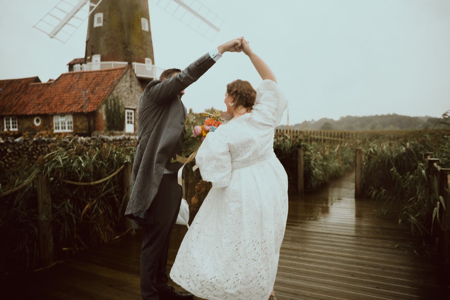 A couple in wedding attire poses romantically in front of a traditional windmill during their countryside celebration.