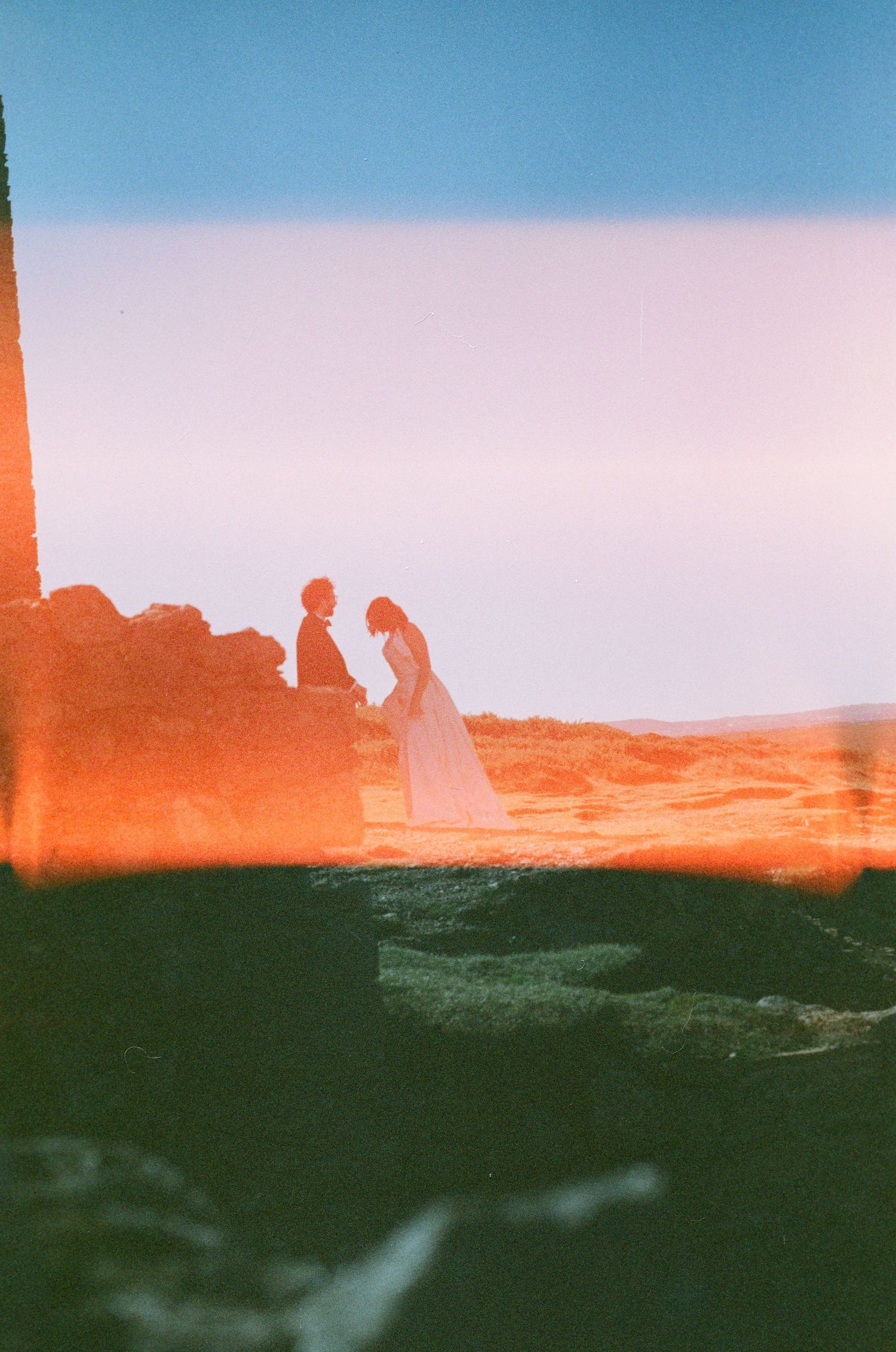 Panoramic view of desert rock formations silhouetted against a colorful sunset sky with orange and blue hues.
