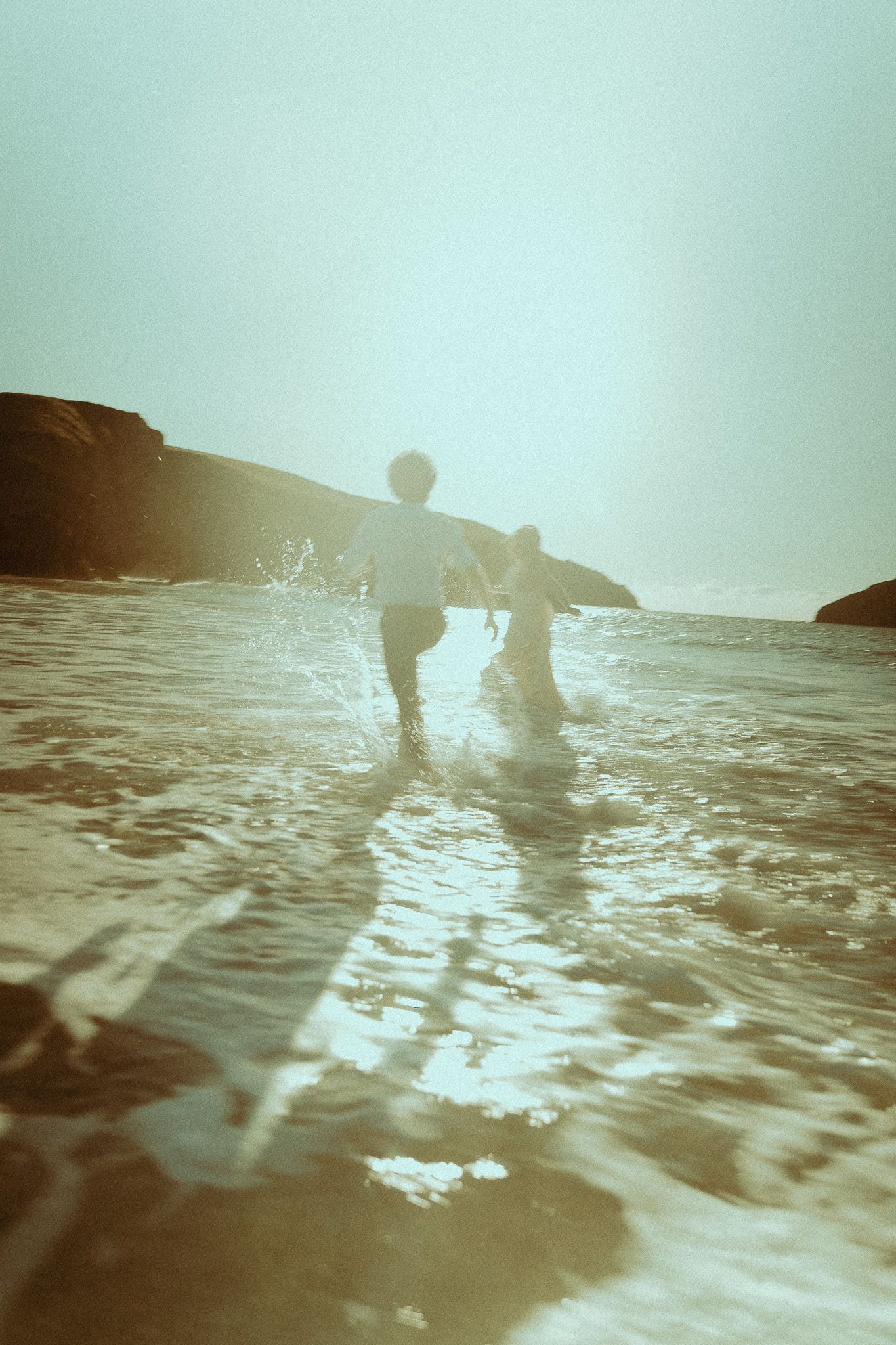 Silhouetted figures play in ocean waves at sunset creating a dreamy, vintage-style sepia photograph.