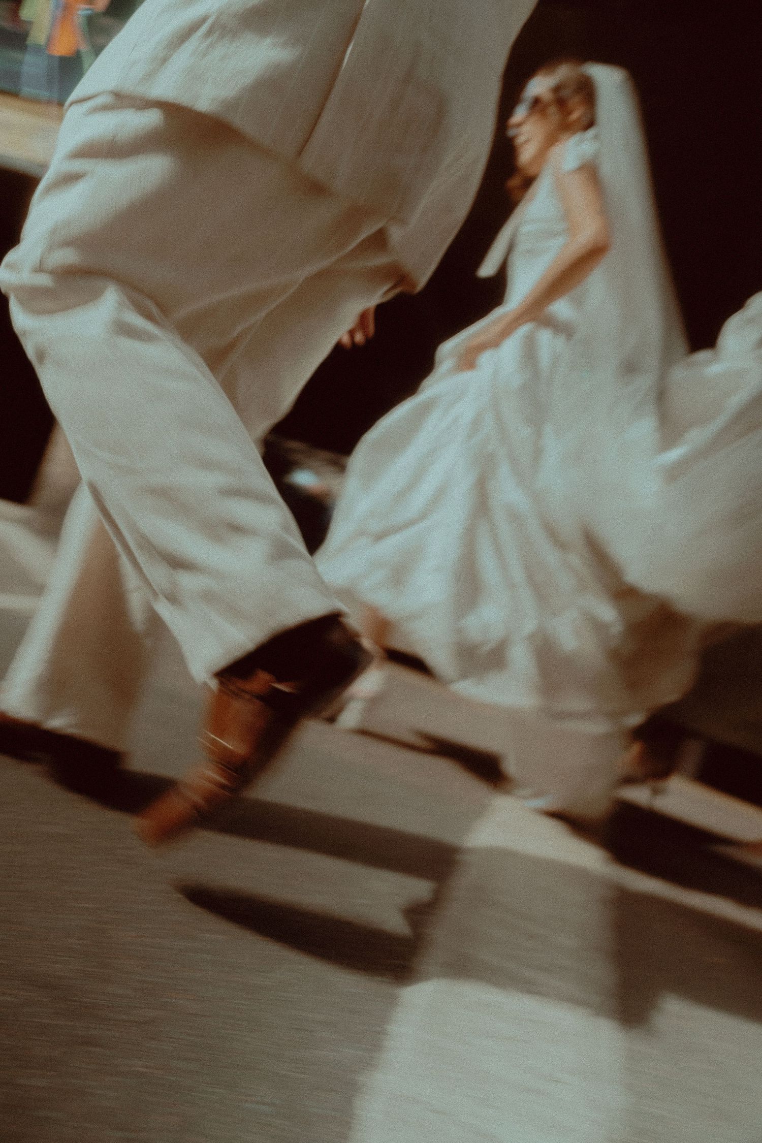 Blurred motion shot of bride in white gown and groom dancing at wedding reception on checkered floor.