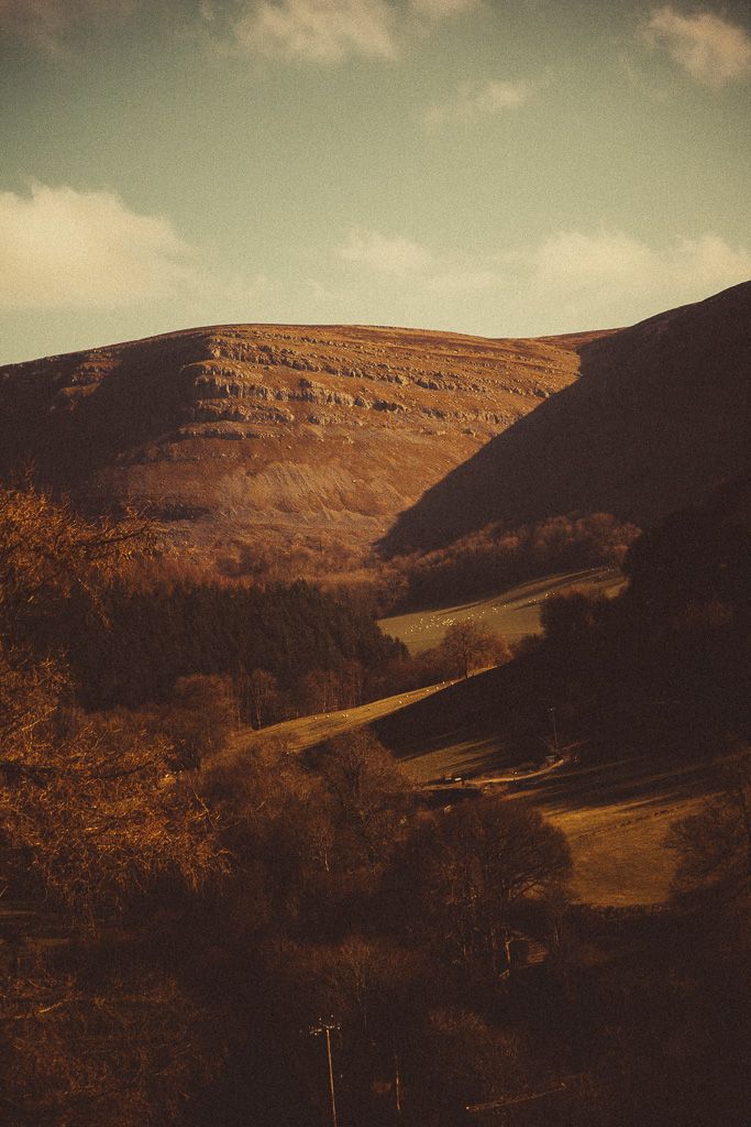 Vintage-toned landscape of rolling hills and autumn trees beneath a partly cloudy sky in a rural valley.