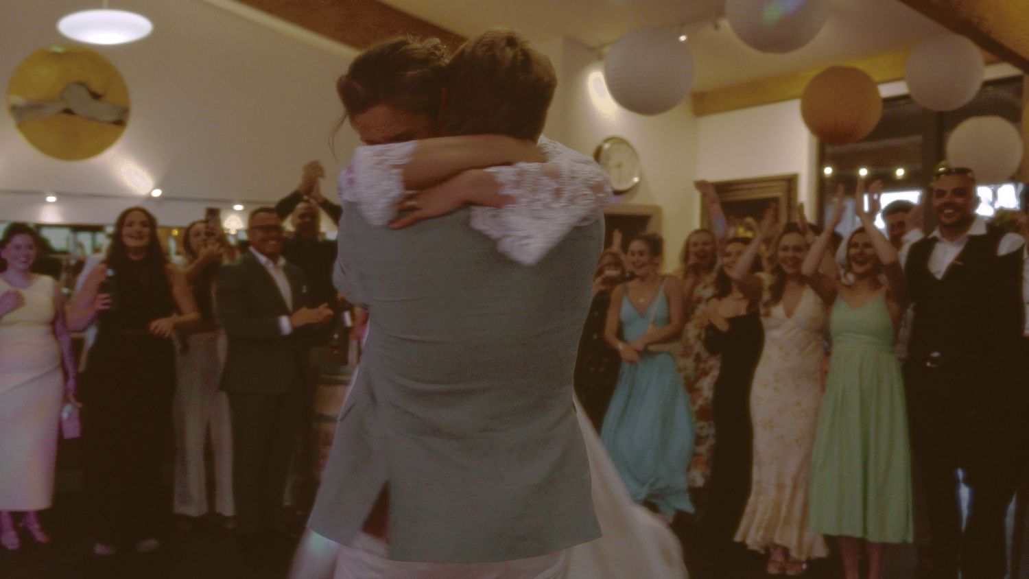 Bride and groom share first dance at wedding reception surrounded by cheering guests in elegant venue.