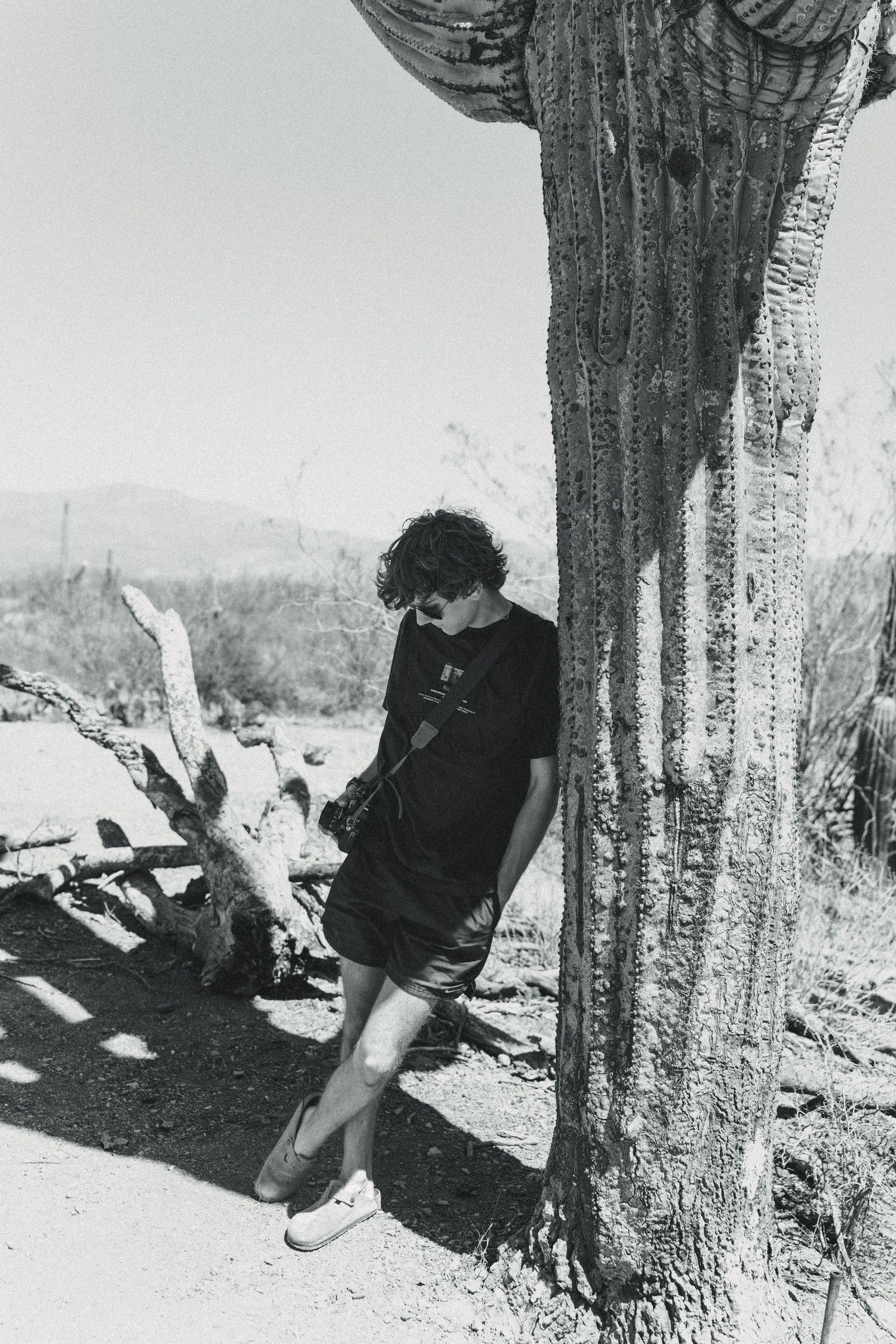 Black and white photo of person leaning against large desert cactus.