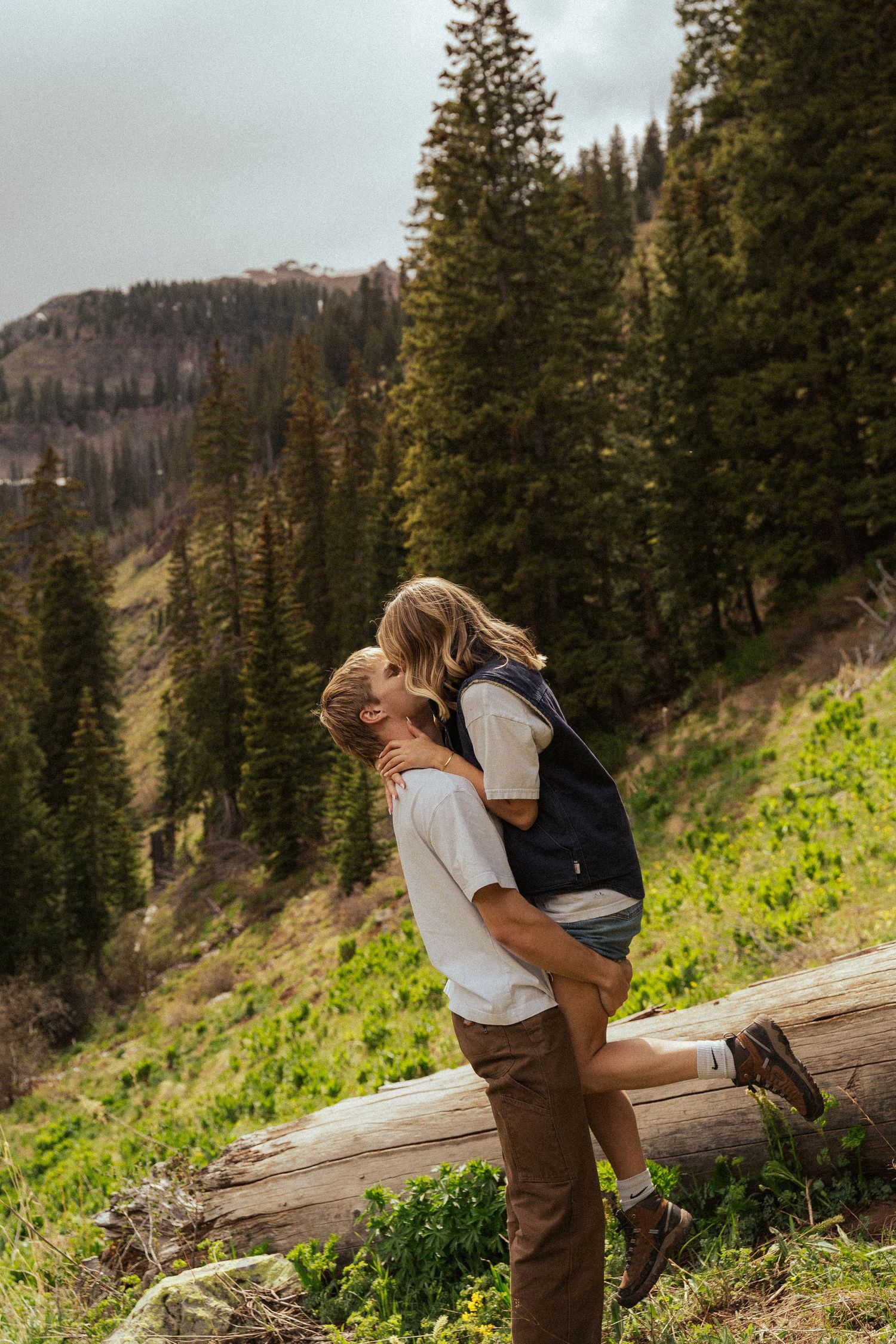 Romantic moment between couple embracing on mountain trail surrounded by evergreen forest and scenic views.