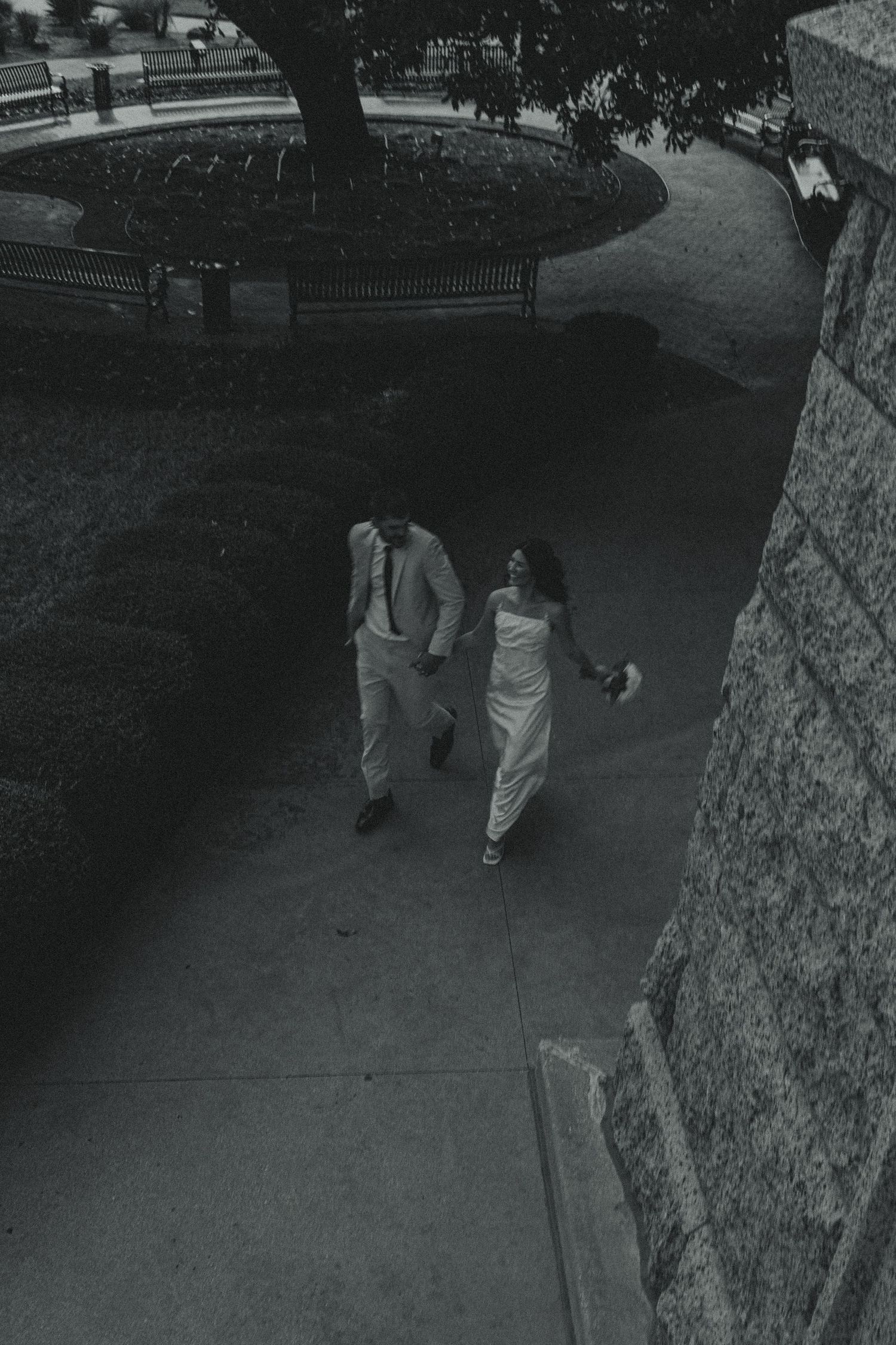 A couple walking down a curved stone path next to a park wall at dusk.