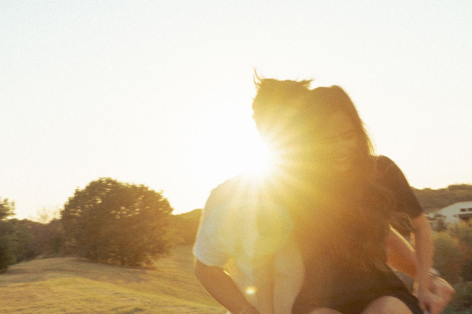 A silhouetted couple embraces in a sunlit grassy field during golden hour.