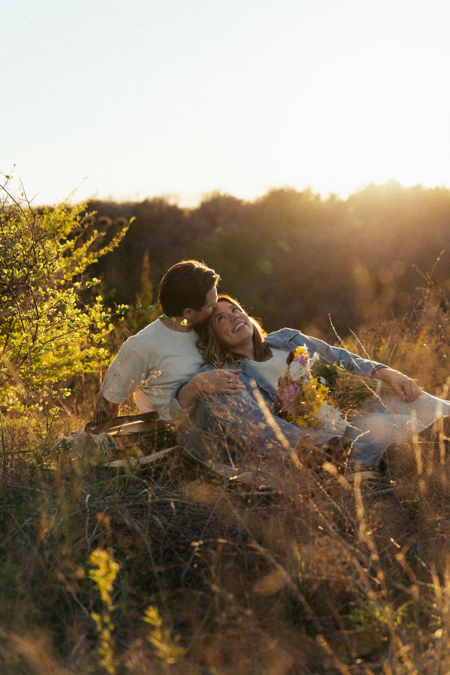 Two people cuddling on blanket in field during golden hour sunset.