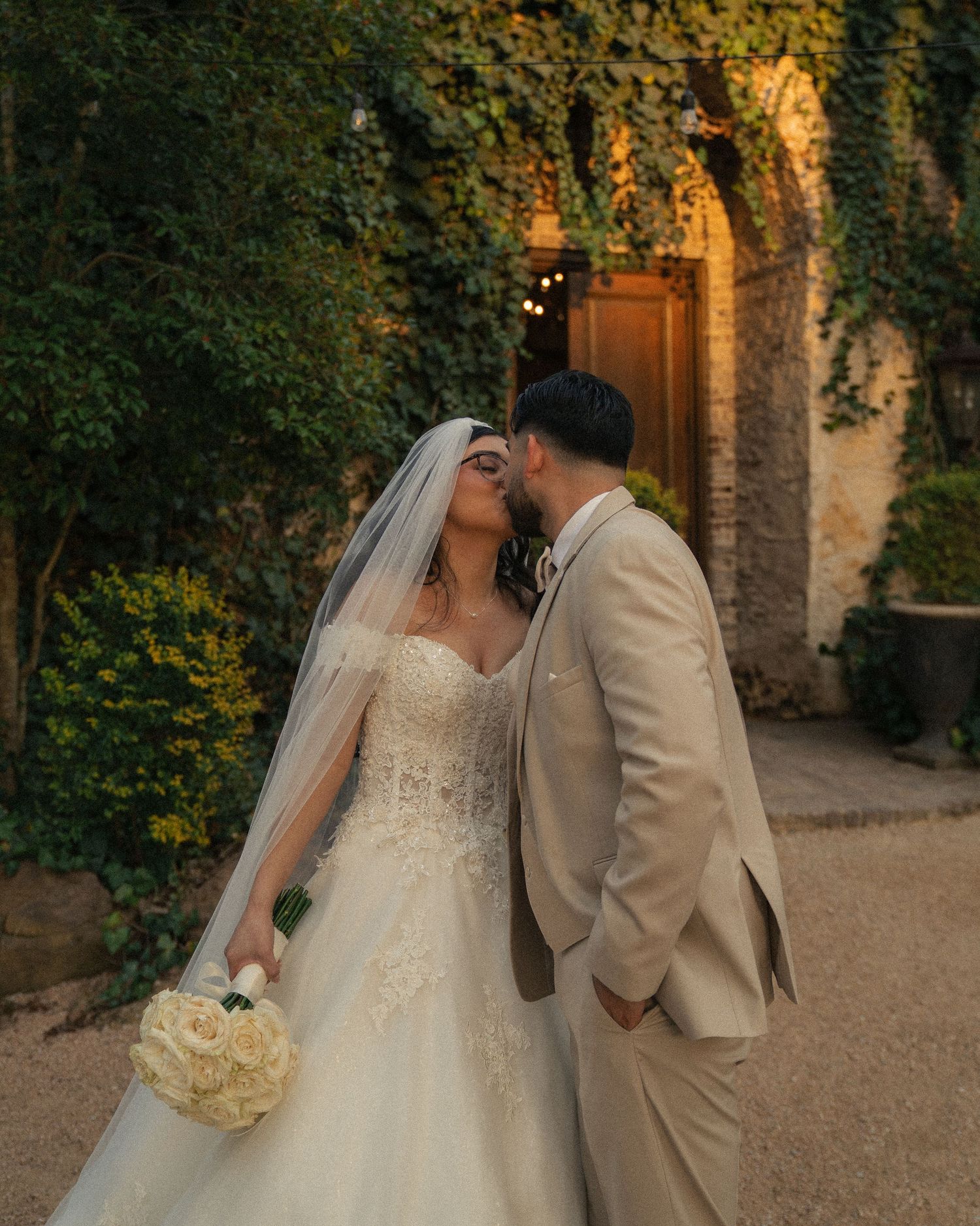 A romantic wedding moment captured in front of an ivy-covered stone archway at golden hour.