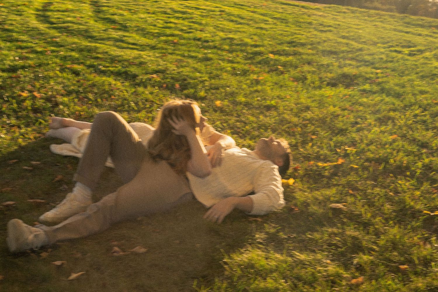 Two people lounging on grass in a sunlit field during sunset.