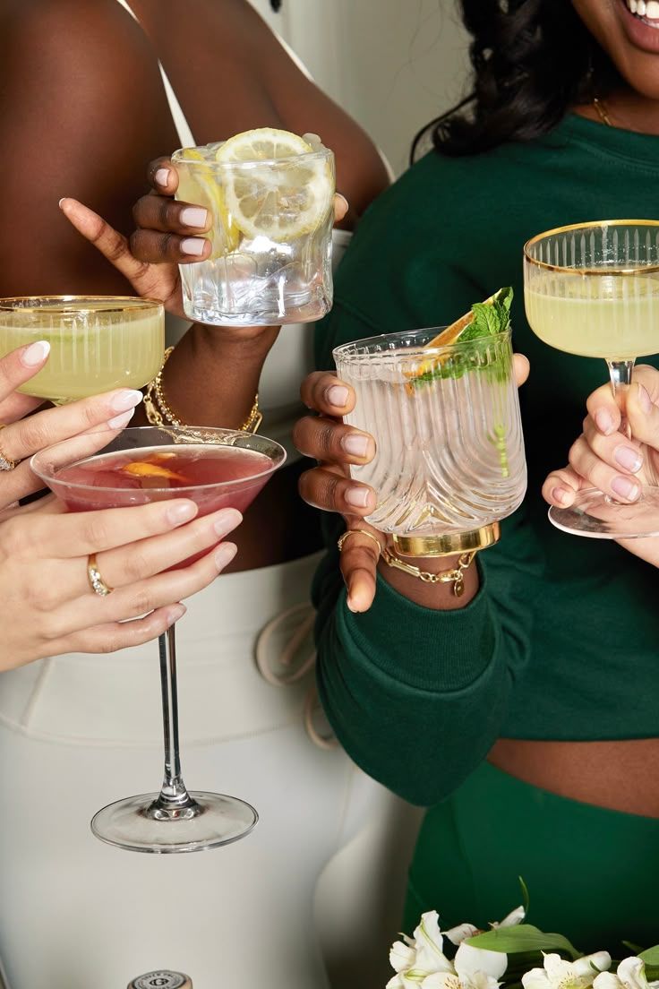 Cocktail glasses filled with margaritas garnished with lime slices and salt rims held by people in green tops.