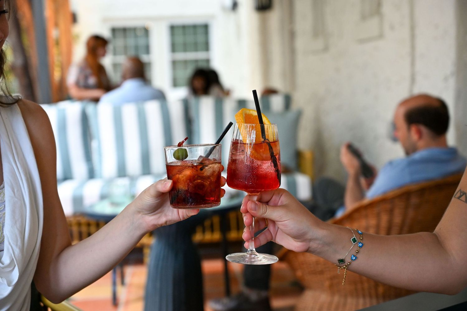 People clinking glasses and toasting with colorful cocktails and beverages at a bar or party.