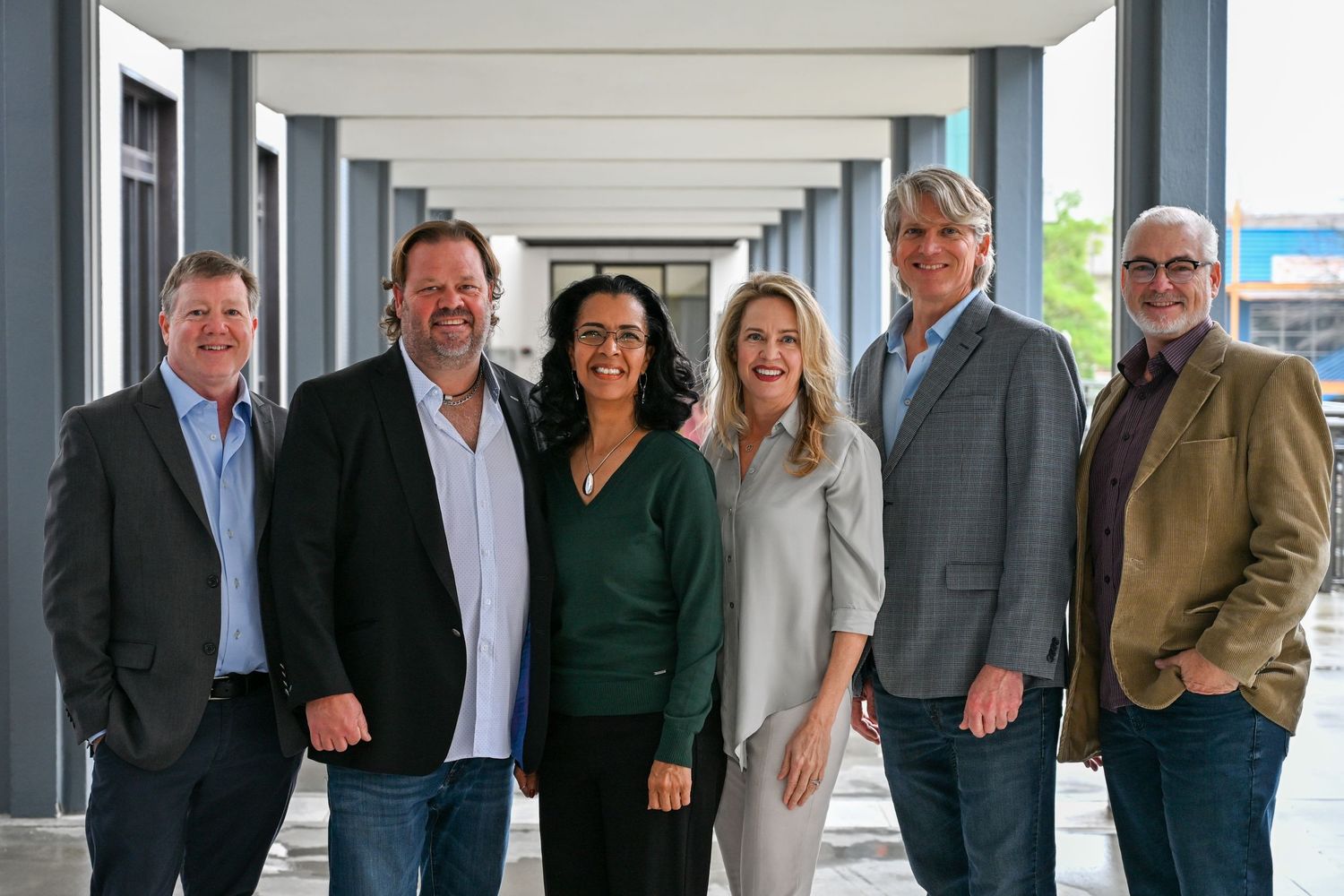 A group of six business professionals standing together on a covered porch area with gray pillars.